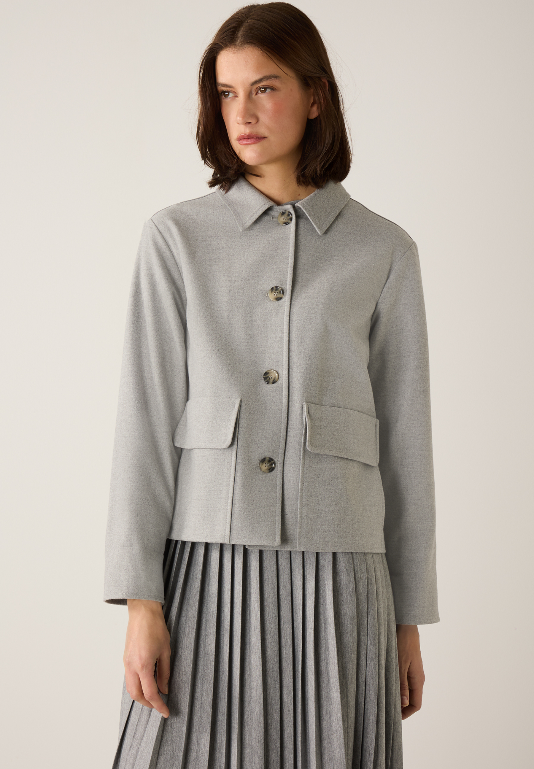 Eine Frau trägt einen grauen MORE & MORE Blazer mit Taschen und Knöpfen.