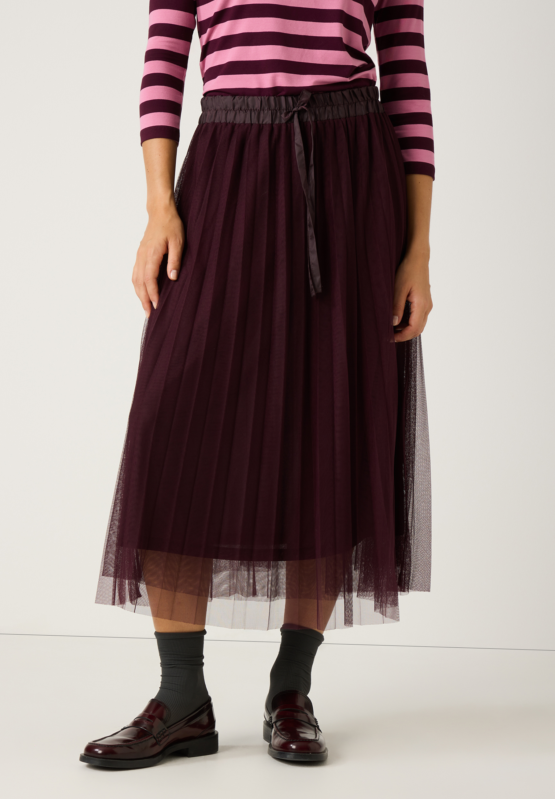 Ein elastischer MORE & MORE Rock mit Mesh-Material in dunklem Lila, kombiniert mit einem gestreiften Oberteil.