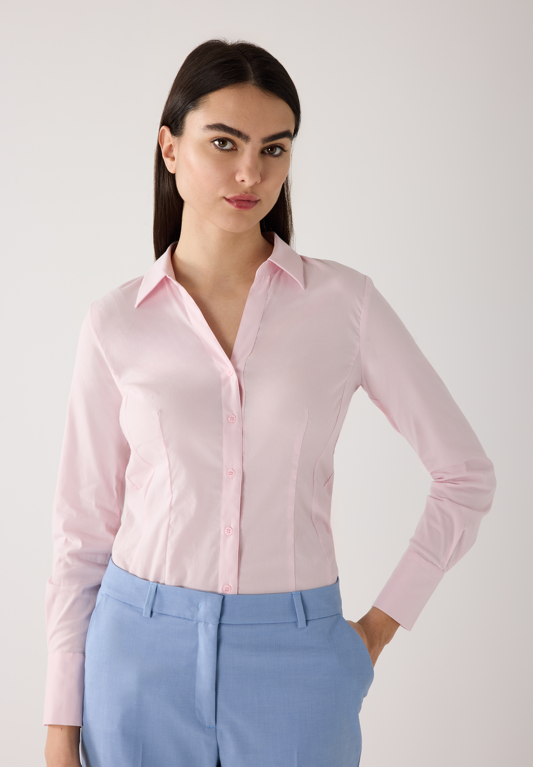 Eine Frau in einem MORE & MORE Oberteil, einer rosa Baumwollmischungsbluse, und einer blauen Hose.