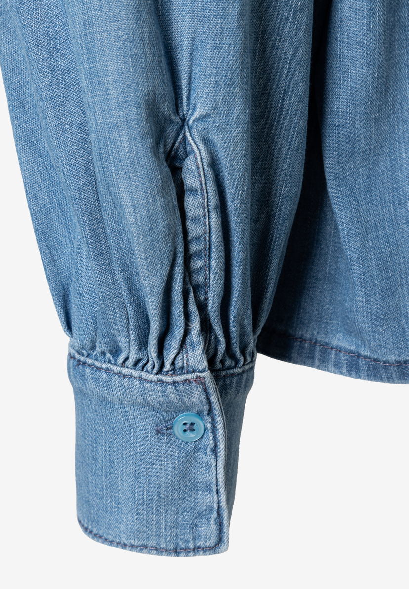 Nahaufnahme eines Ärmels der MORE & MORE Bluse aus Denim mit Knopf. Nahaufnahme eines Ärmels der MORE & MORE Bluse aus Denim mit Knopf.