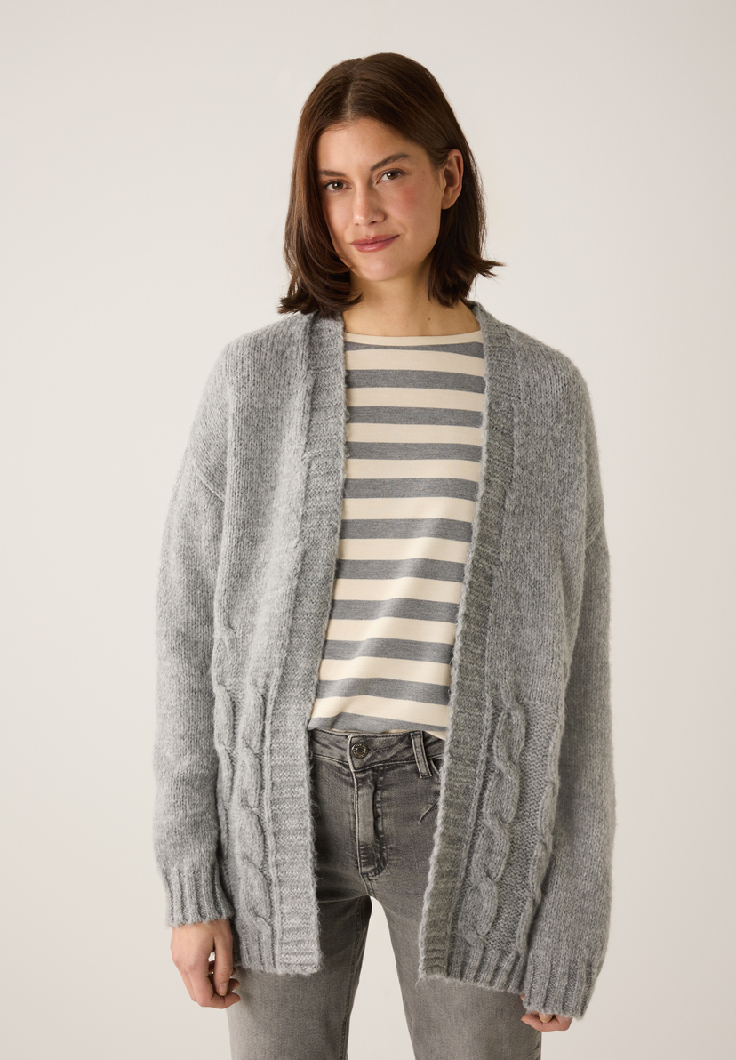 Eine Frau trägt eine Strickjacke von MORE & MORE über einem gestreiften Oberteil und graue Jeans. Eine Frau trägt eine Strickjacke von MORE & MORE über einem gestreiften Oberteil und graue Jeans.