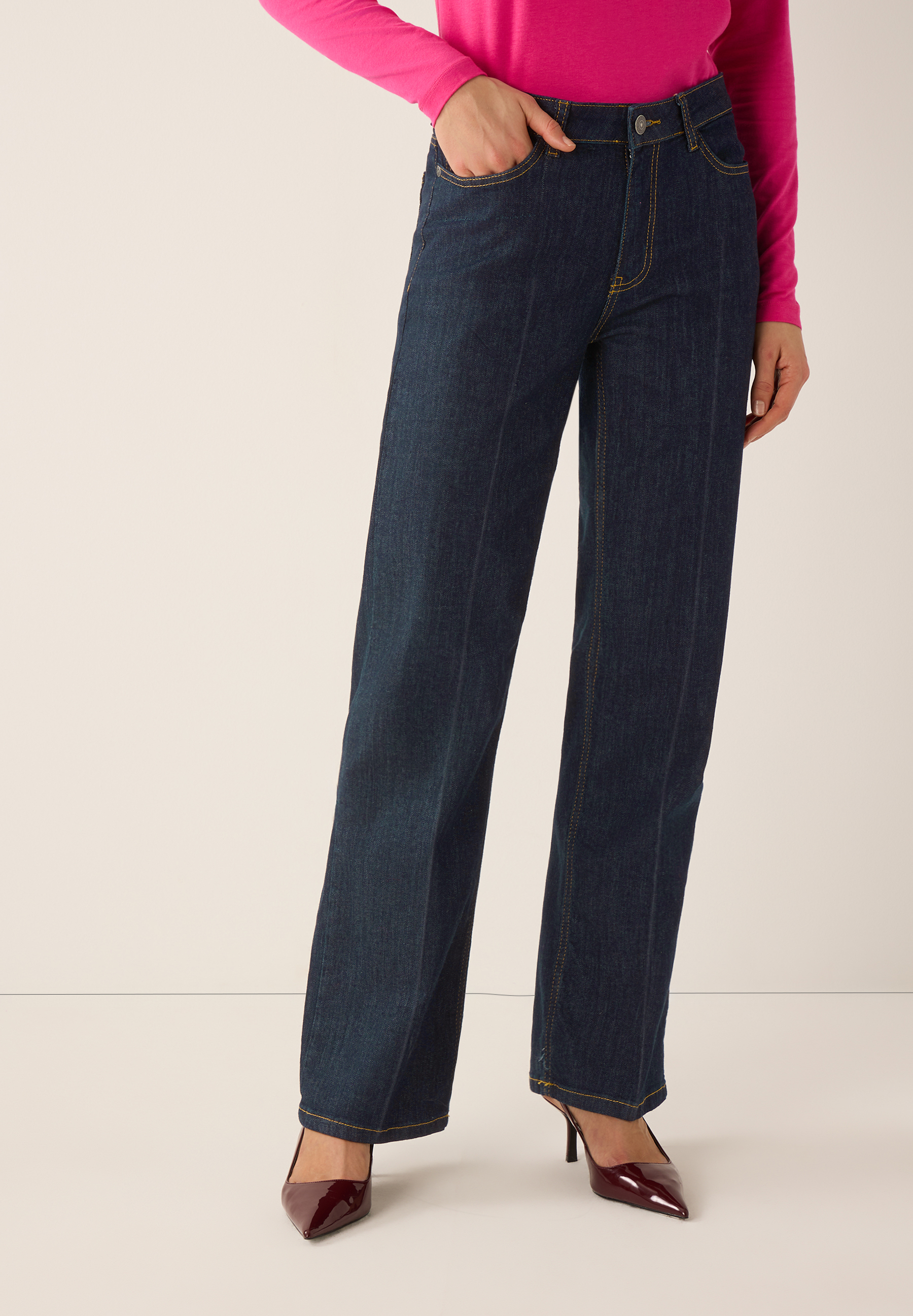 Eine Frau in MORE & MORE Jeans, aus Denim und mit angenehmem Tragekomfort, kombiniert mit einem pinken Oberteil und roten High Heels.
