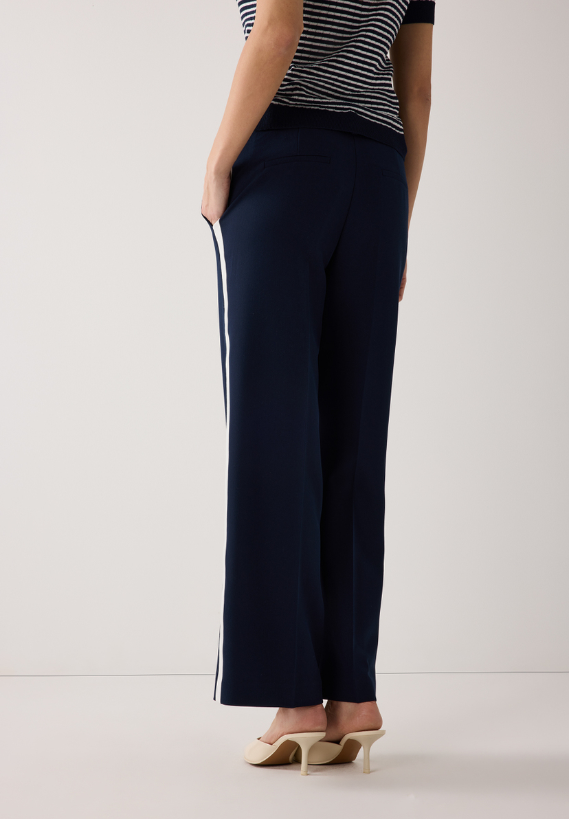 Marineblaue MORE & MORE Hose mit weißem Seitenstreifen und beigen Mules von hinten. Marineblaue MORE & MORE Hose mit weißem Seitenstreifen und beigen Mules von hinten.