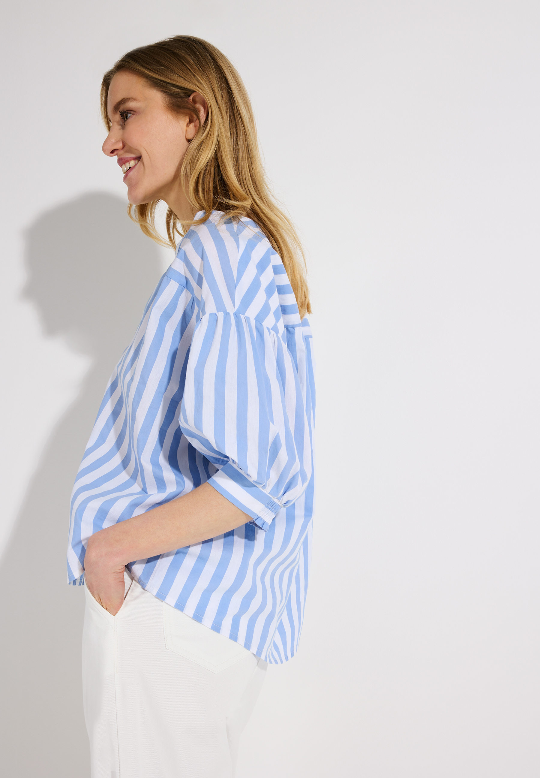 Eine Frau in einer blau-weiß gestreiften MORE & MORE Bluse aus Popeline. Eine Frau in einer blau-weiß gestreiften MORE & MORE Bluse aus Popeline.