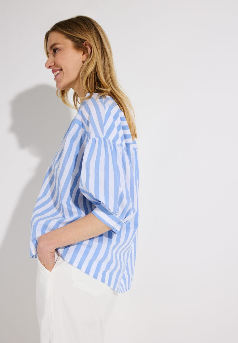 Eine Frau in einer blau-weiß gestreiften MORE & MORE Bluse aus Popeline. Eine Frau in einer blau-weiß gestreiften MORE & MORE Bluse aus Popeline.