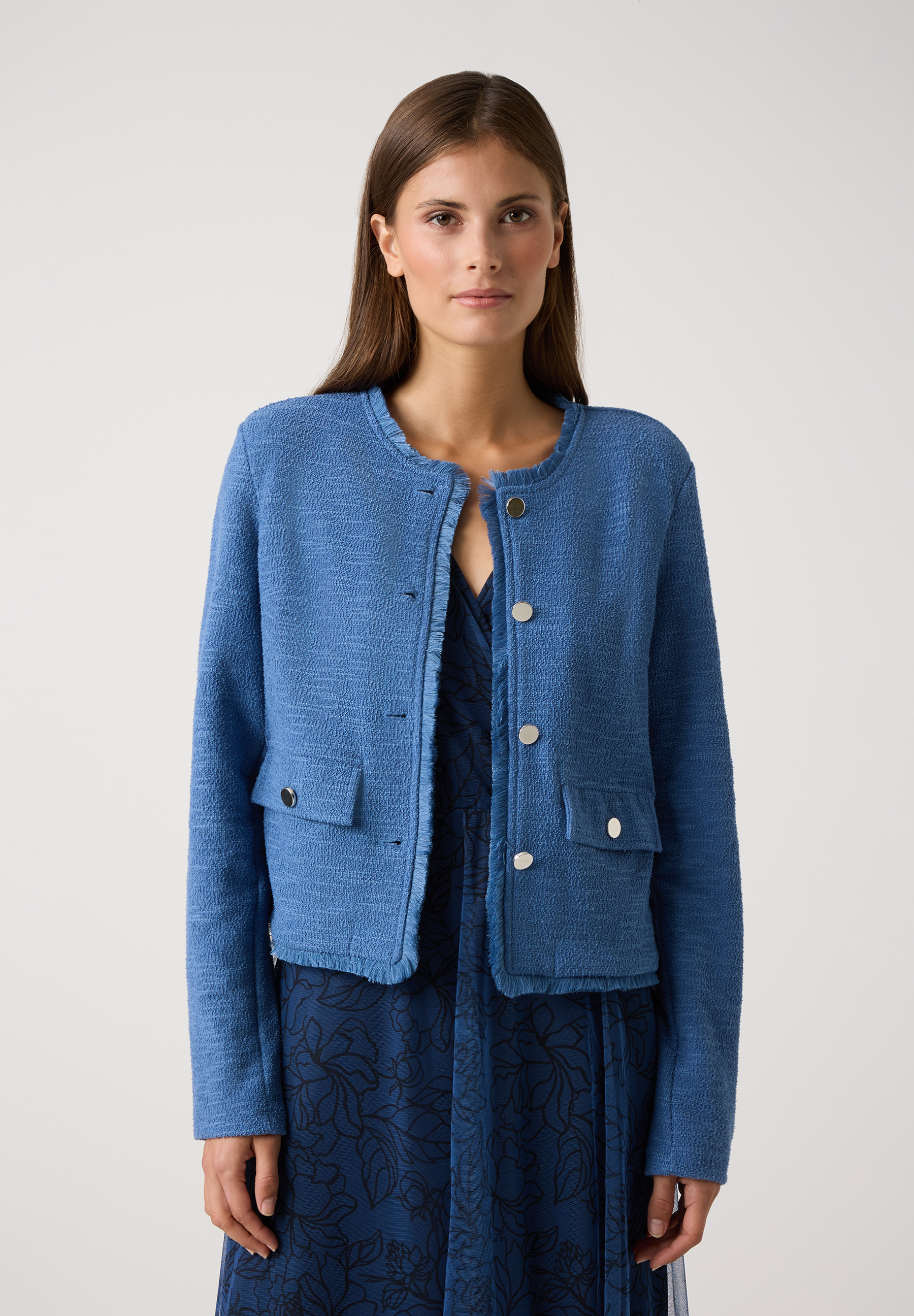 Eine Frau trägt einen blauen MORE & MORE Blazer mit Strukturjersey über einem blauen Kleid.