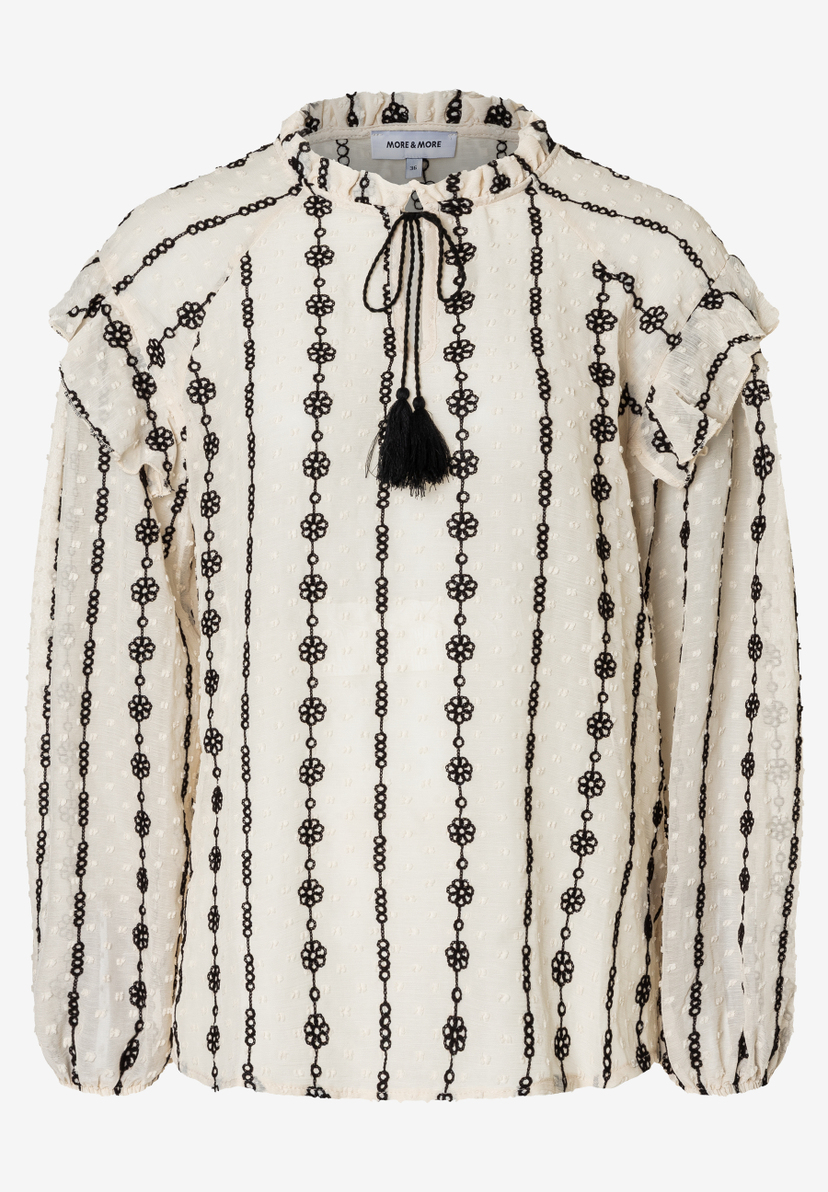 Eine MORE & MORE Bluse in Creme mit schwarzen Blumenketten, Rüschen und Quasten. Eine MORE & MORE Bluse in Creme mit schwarzen Blumenketten, Rüschen und Quasten.