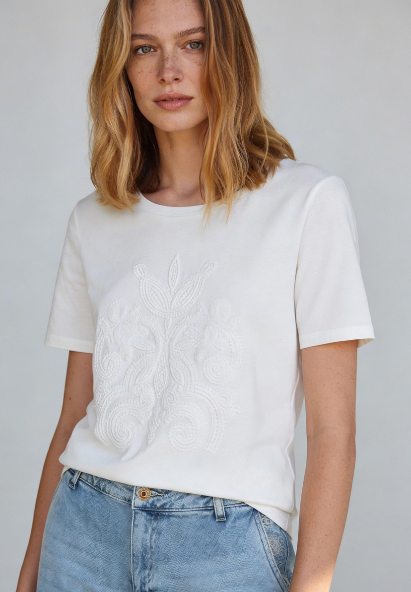 Eine Frau trägt ein weißes MORE & MORE T-Shirt mit dekorativer Stickerei und Jeans. Eine Frau trägt ein weißes MORE & MORE T-Shirt mit dekorativer Stickerei und Jeans.