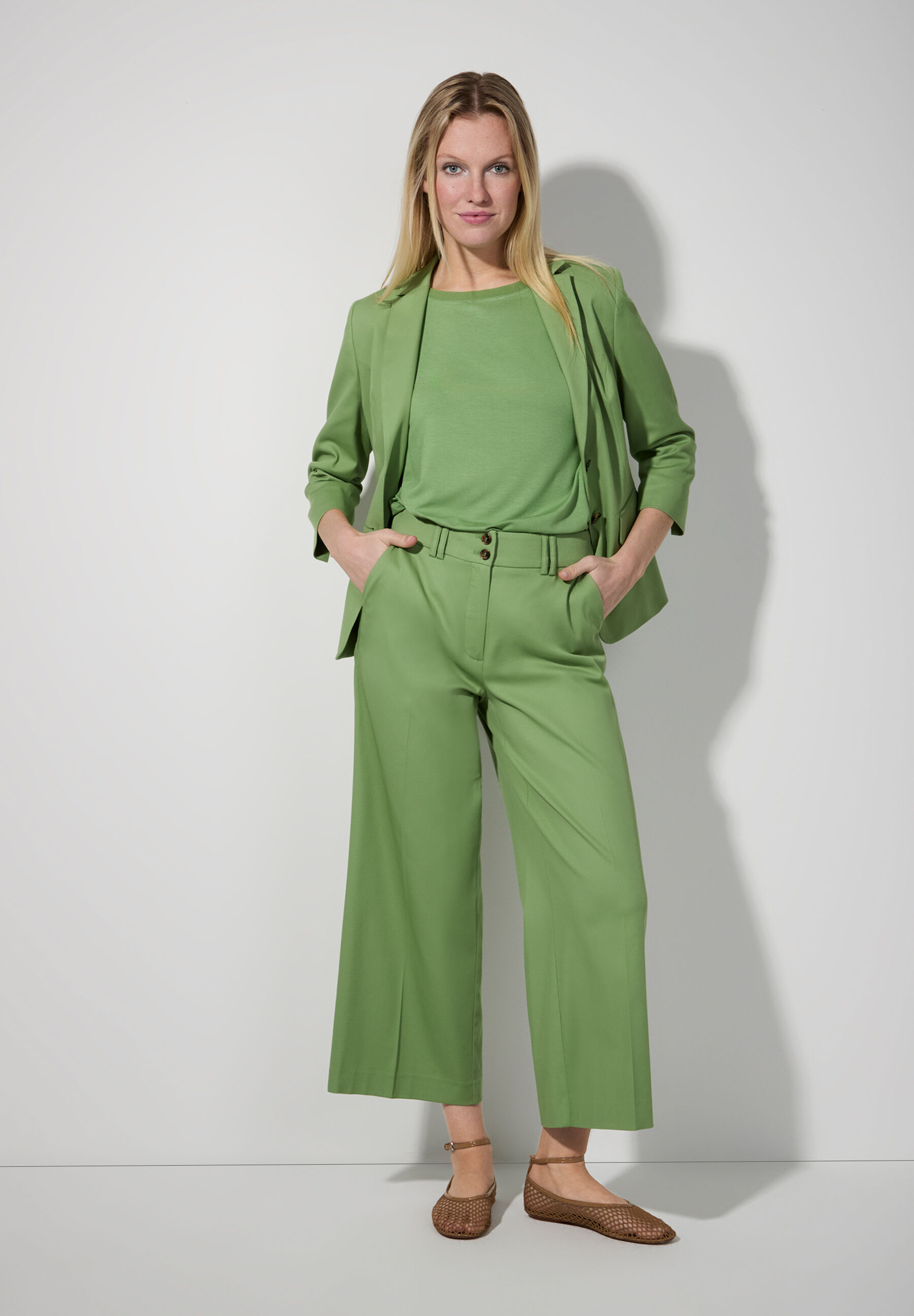 Eine Frau in einem grünen MORE & MORE Blazer und passender Hose vor hellem Hintergrund. Eine Frau in einem grünen MORE & MORE Blazer und passender Hose vor hellem Hintergrund.