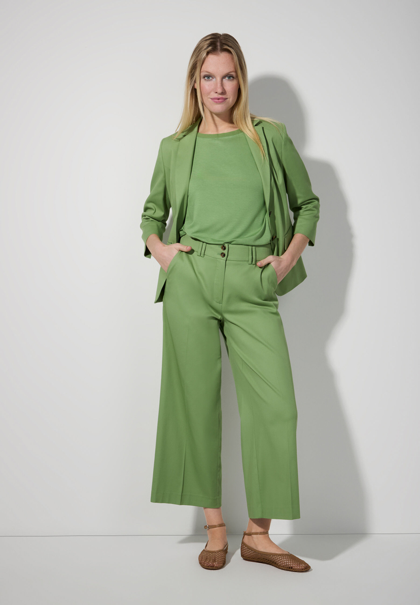 Eine Frau in einem grünen MORE & MORE Blazer und passender Hose vor hellem Hintergrund. Eine Frau in einem grünen MORE & MORE Blazer und passender Hose vor hellem Hintergrund.