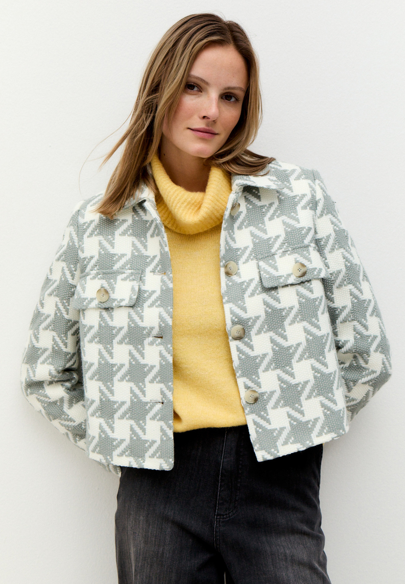 Eine Frau trägt einen Blazer von MORE & MORE mit Sternenmuster über einem gelben Rollkragenpullover. Eine Frau trägt einen Blazer von MORE & MORE mit Sternenmuster über einem gelben Rollkragenpullover.