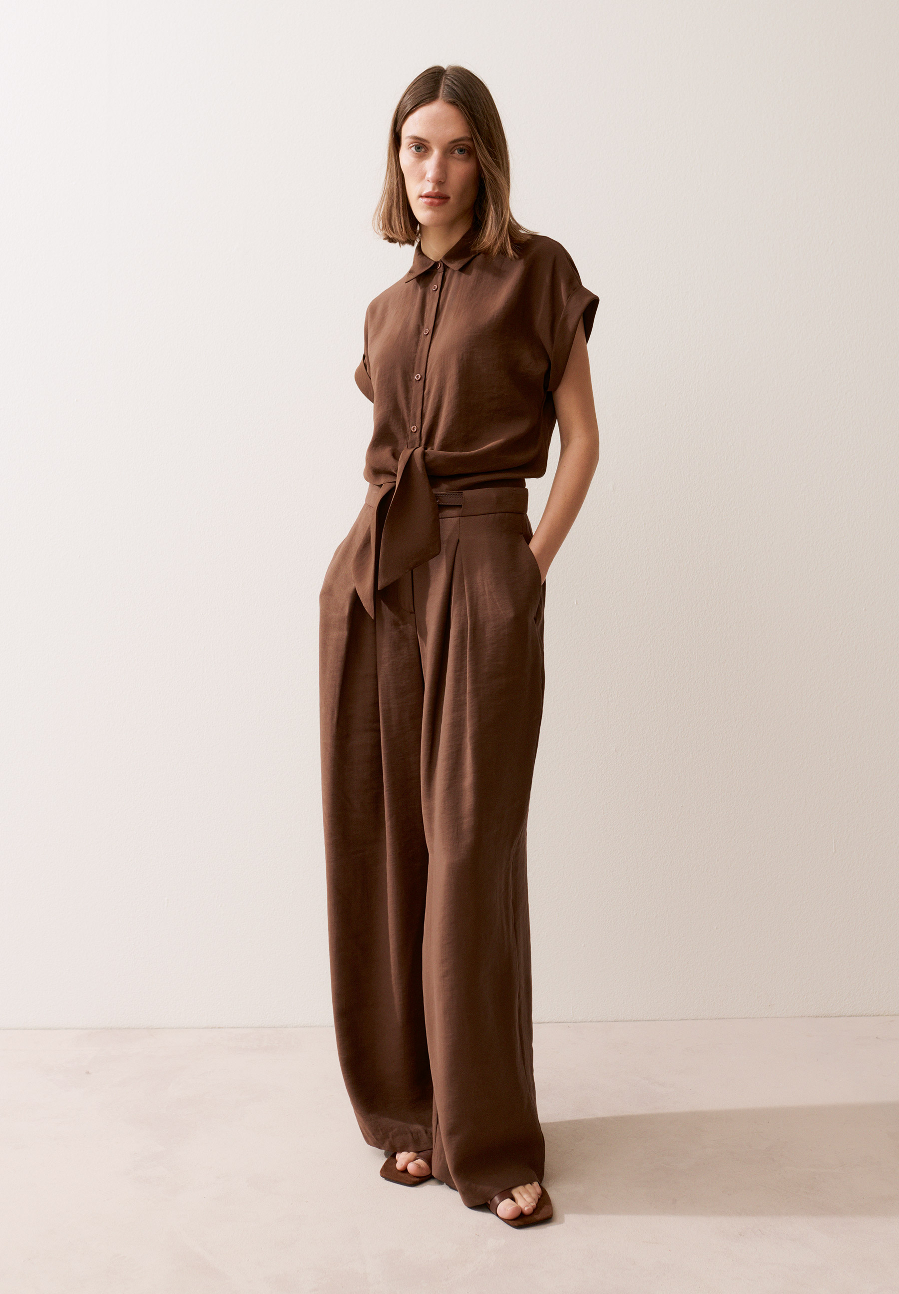 Eine Frau im MORE & MORE-Ensemble aus brauner Bluse und Hose, lässig und stilvoll.