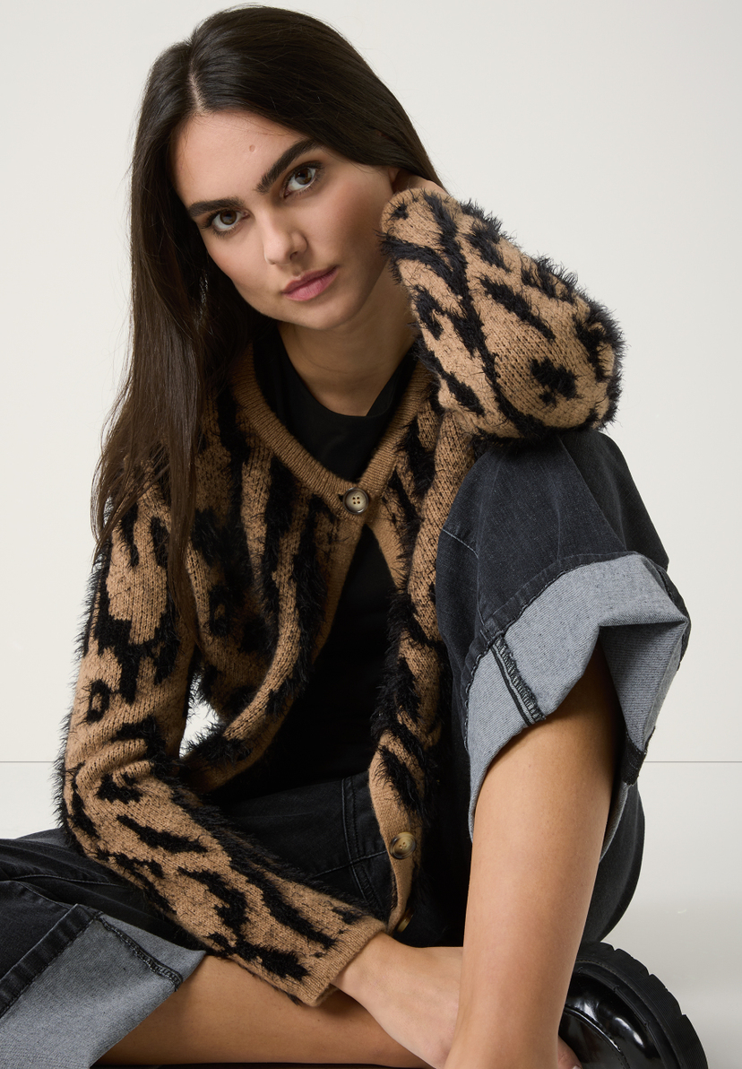 Eine Frau mit einem Strickoberteil von MORE & MORE mit wärmendem Leopardenmuster und passender Hose sitzt lässig da. Eine Frau mit einem Strickoberteil von MORE & MORE mit wärmendem Leopardenmuster und passender Hose sitzt lässig da.