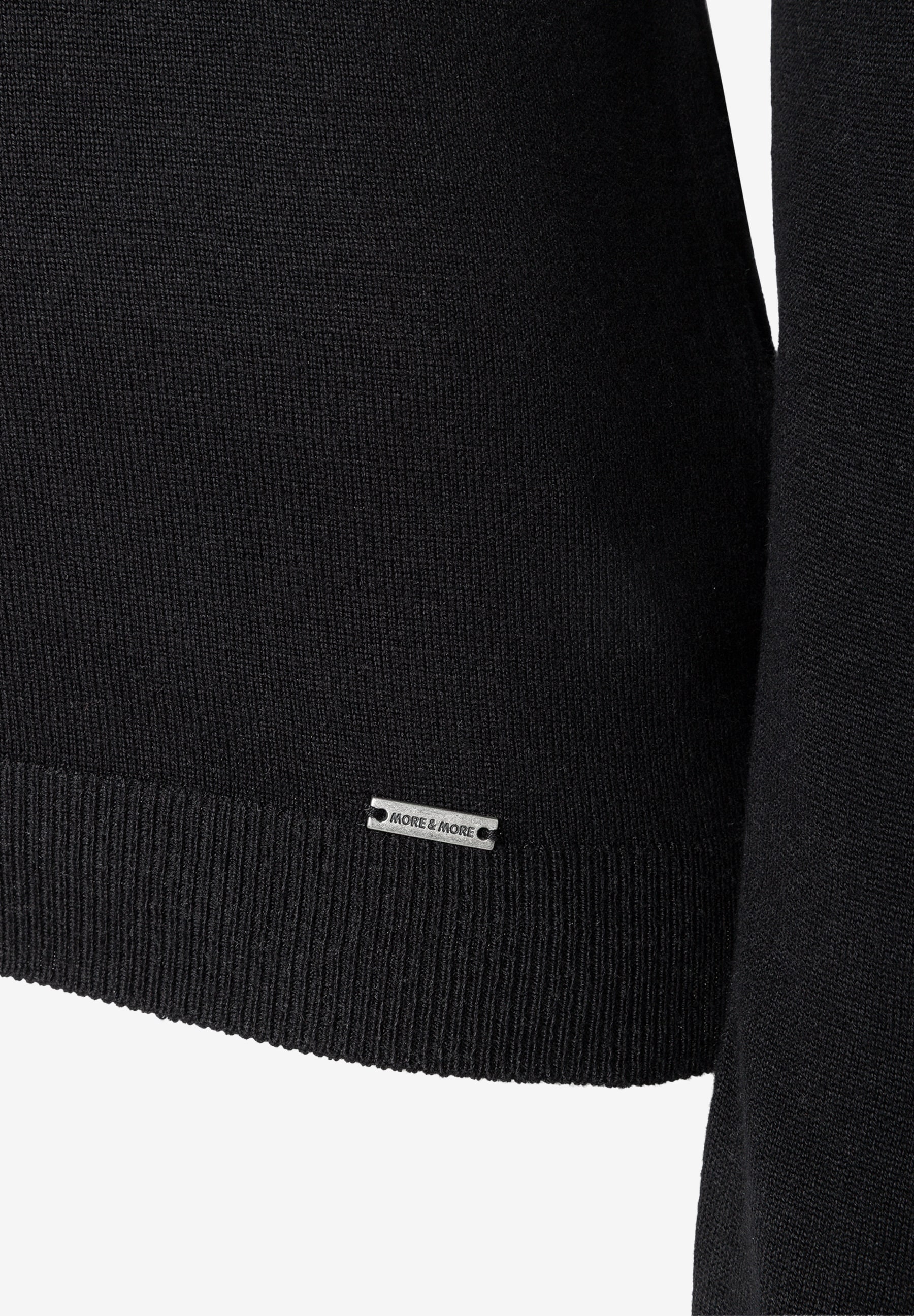 MORE & MORE Feinstrick-Pullover in Schwarz. Nahaufnahme des Saums mit dezentem Markenetikett. MORE & MORE Feinstrick-Pullover in Schwarz. Nahaufnahme des Saums mit dezentem Markenetikett.