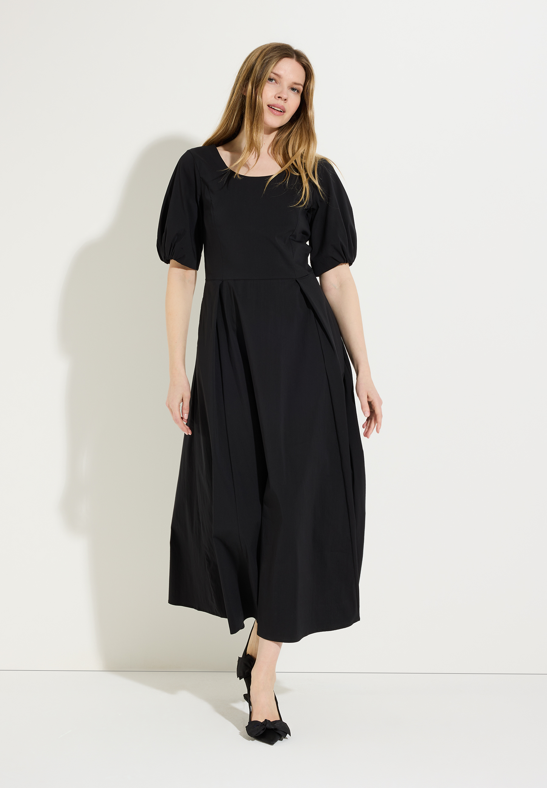 Eine Frau präsentiert ein schwarzes Kleid von MORE & MORE mit Popeline und Puffärmeln vor hellem Hintergrund.