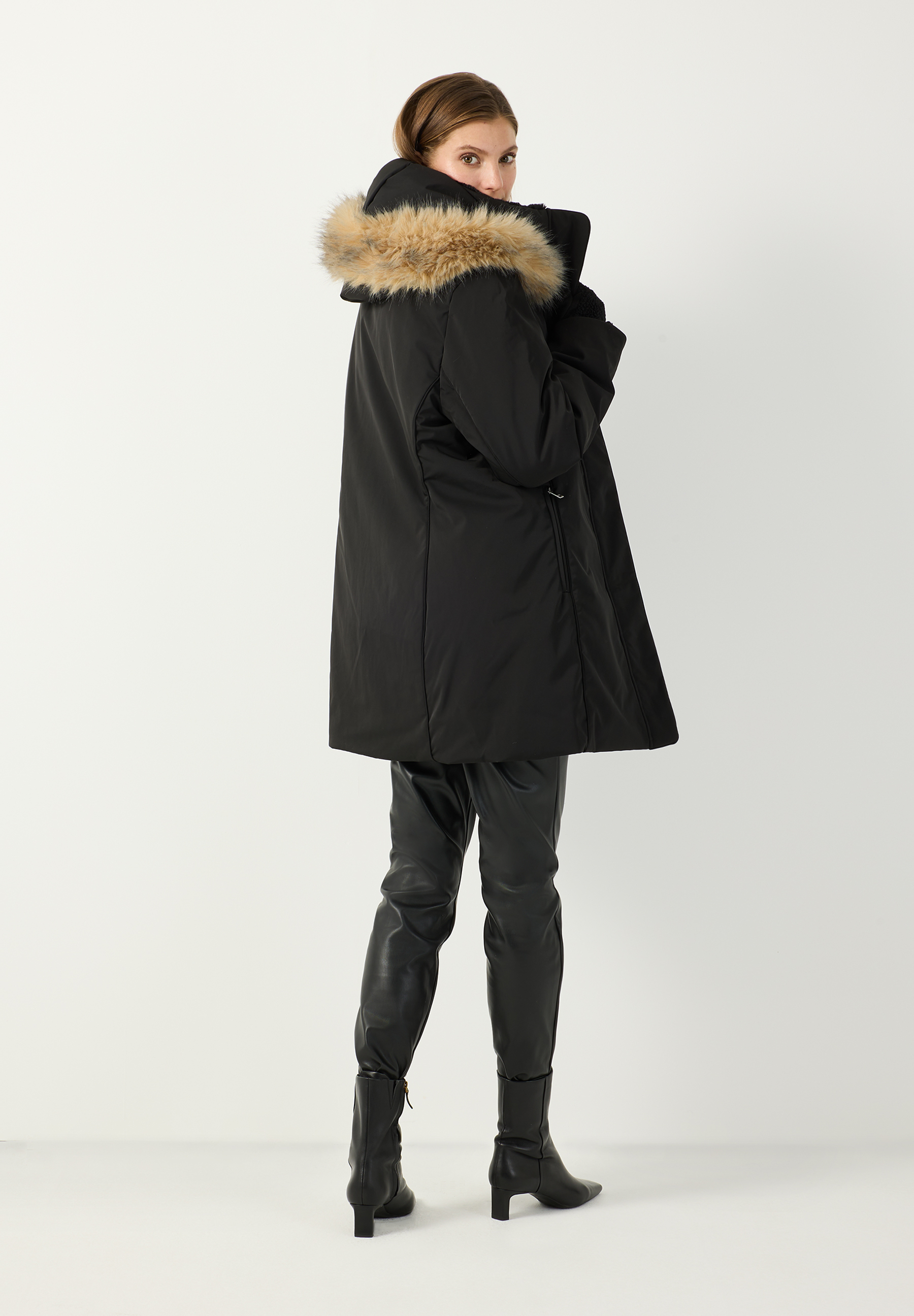 MORE & MORE schwarzer Parka mit Kapuze, Pelzbesatz und blauer Jeans auf einer Frau, die ihre Hände in den Taschen hält. MORE & MORE schwarzer Parka mit Kapuze, Pelzbesatz und blauer Jeans auf einer Frau, die ihre Hände in den Taschen hält.