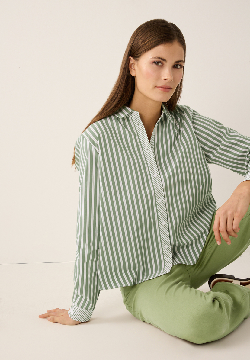 Eine Frau in einer gestreiften Popeline-Bluse von MORE & MORE posiert. Eine Frau in einer gestreiften Popeline-Bluse von MORE & MORE posiert.