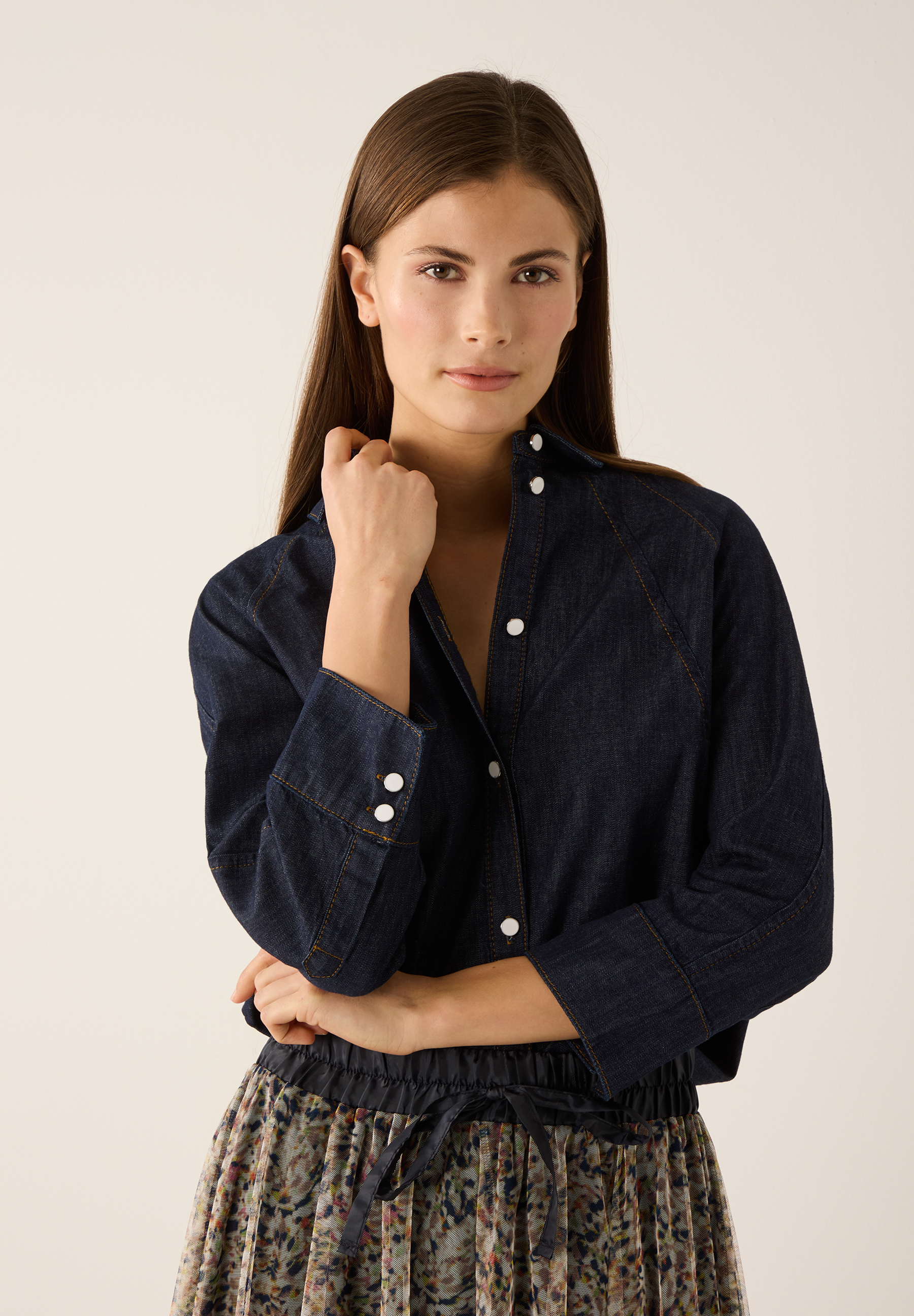 Eine Frau trägt eine MORE & MORE Bluse aus Denim und einen Rock mit Blumenmuster vor einem hellen Hintergrund.