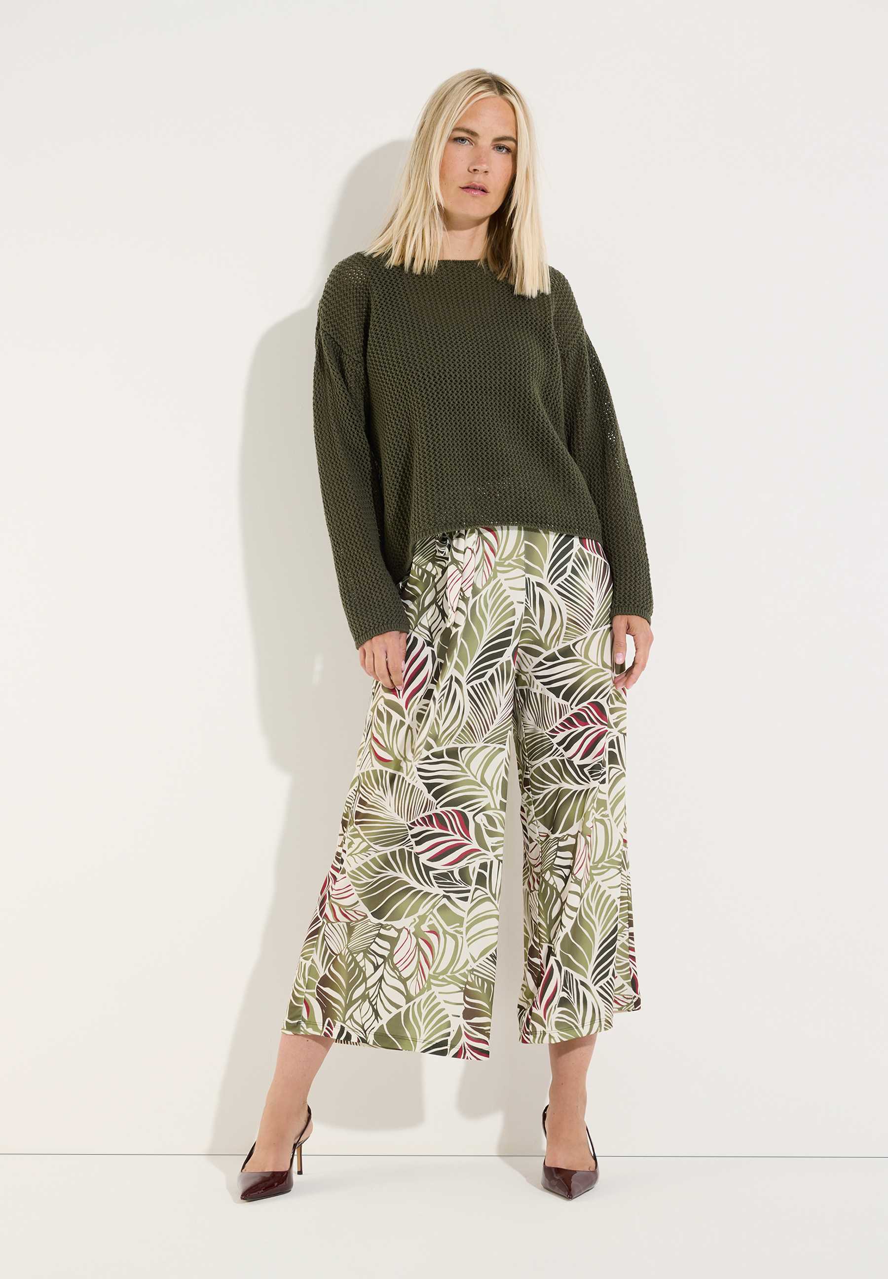 MORE & MORE Pullover: Eine blonde Frau trägt einen khakifarbenen Pullover und eine Hose mit Blättermuster. MORE & MORE Pullover: Eine blonde Frau trägt einen khakifarbenen Pullover und eine Hose mit Blättermuster.