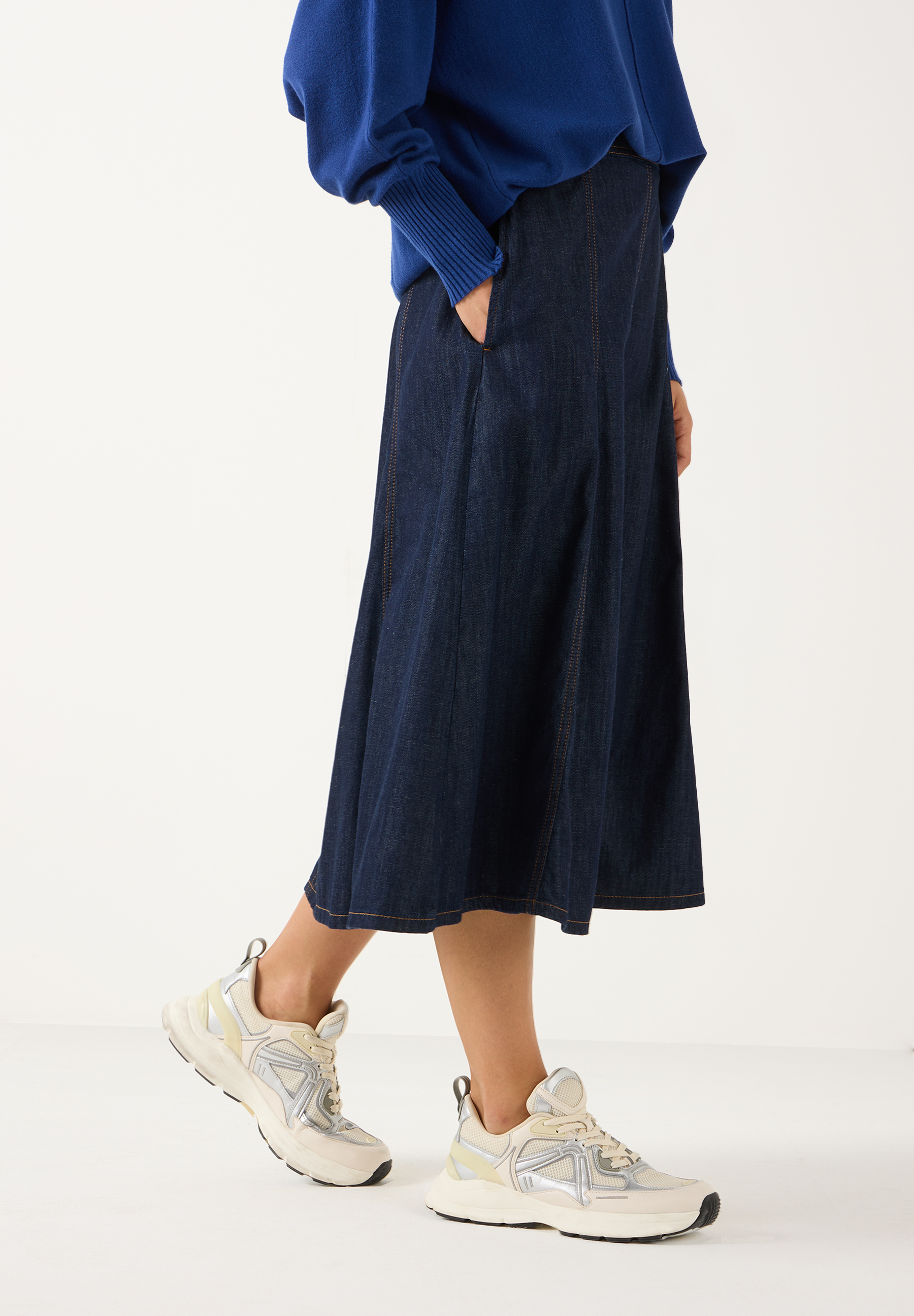 MORE & MORE Midirock aus hautfreundlichem Denim in Dunkelblau, kombiniert mit einem blauen Strickpullover und Sneakers. MORE & MORE Midirock aus hautfreundlichem Denim in Dunkelblau, kombiniert mit einem blauen Strickpullover und Sneakers.