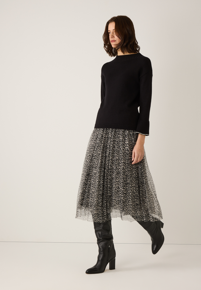 Eine Frau trägt einen schwarzen MORE & MORE Strickpullover, einen Rock und Stiefel vor einem hellen Hintergrund. Eine Frau trägt einen schwarzen MORE & MORE Strickpullover, einen Rock und Stiefel vor einem hellen Hintergrund.