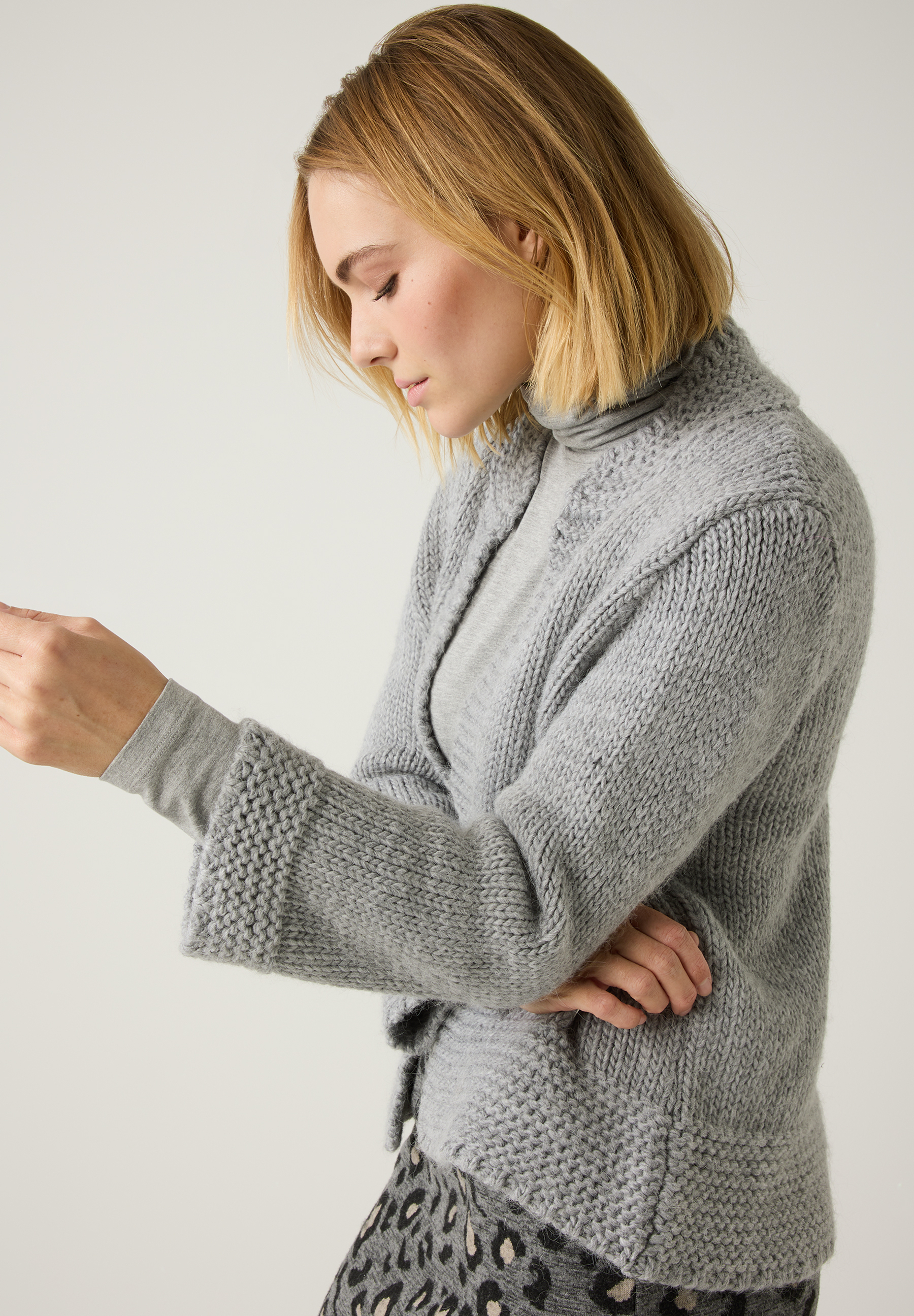 Eine Frau mit blondem Haar trägt einen grauen Strickpullover der Marke MORE & MORE. Das Material ist angenehm und wärmend. Eine Frau mit blondem Haar trägt einen grauen Strickpullover der Marke MORE & MORE. Das Material ist angenehm und wärmend.