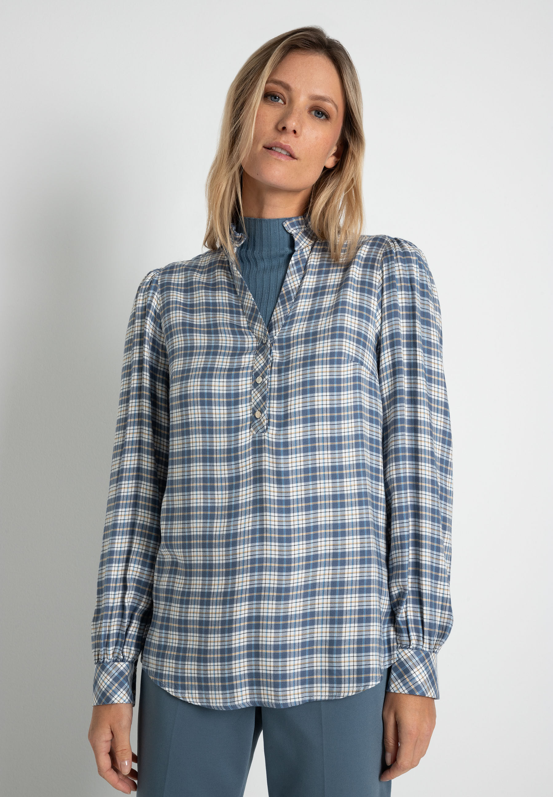 Eine Frau trägt eine blau-weiß karierte MORE & MORE Bluse mit langen Ärmeln und einen Rollkragenpullover.