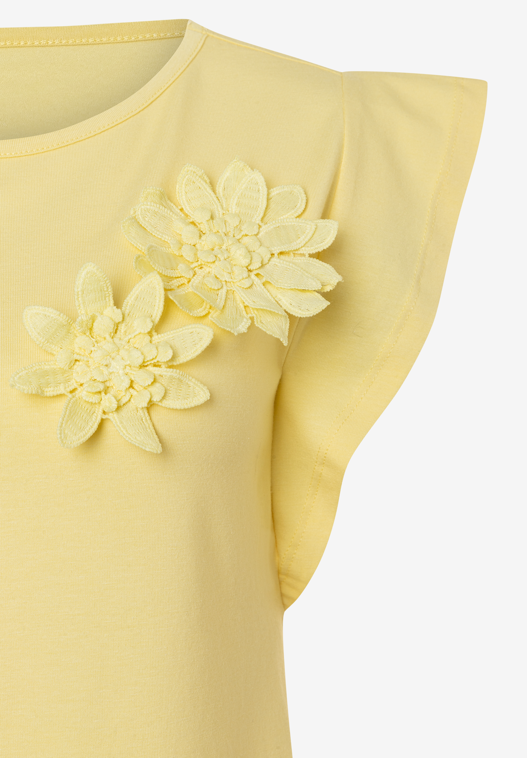 Nahaufnahme eines gelben MORE & MORE T-Shirts mit zwei floralen Applikationen. Nahaufnahme eines gelben MORE & MORE T-Shirts mit zwei floralen Applikationen.