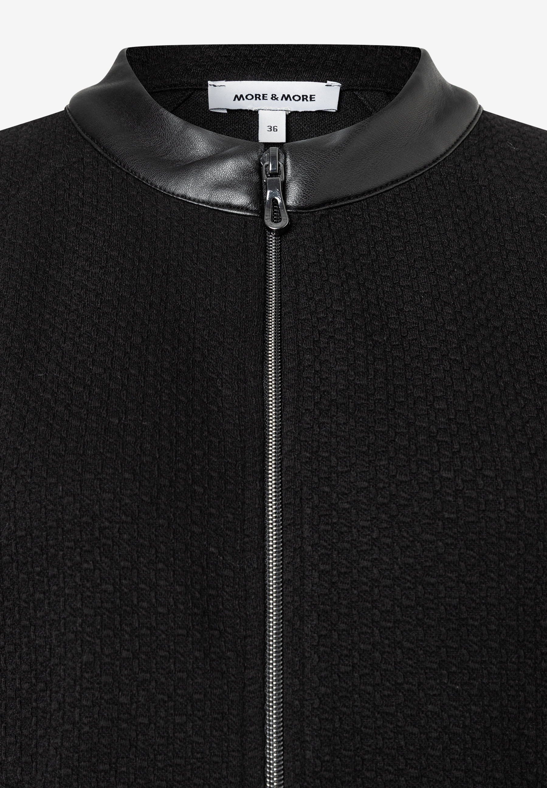 Nahaufnahme eines schwarzen MORE & MORE Oberteils mit Kunstleder-Kragen und Reißverschluss. Nahaufnahme eines schwarzen MORE & MORE Oberteils mit Kunstleder-Kragen und Reißverschluss.