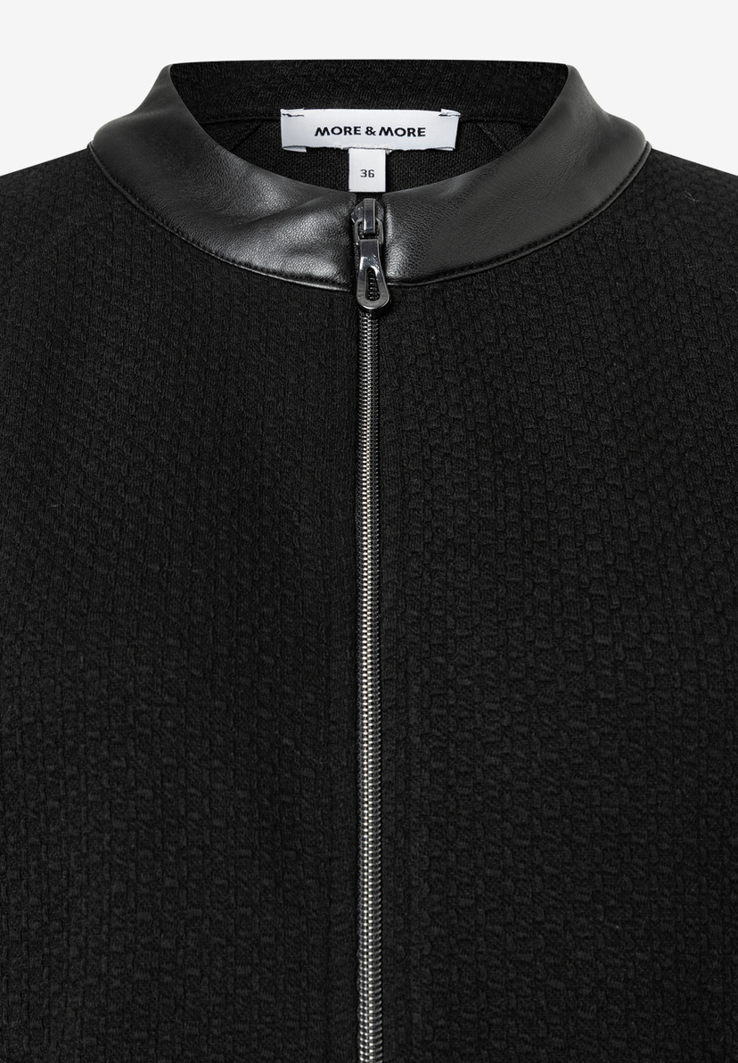 Nahaufnahme eines schwarzen MORE & MORE Oberteils mit Kunstleder-Kragen und Reißverschluss. Nahaufnahme eines schwarzen MORE & MORE Oberteils mit Kunstleder-Kragen und Reißverschluss.