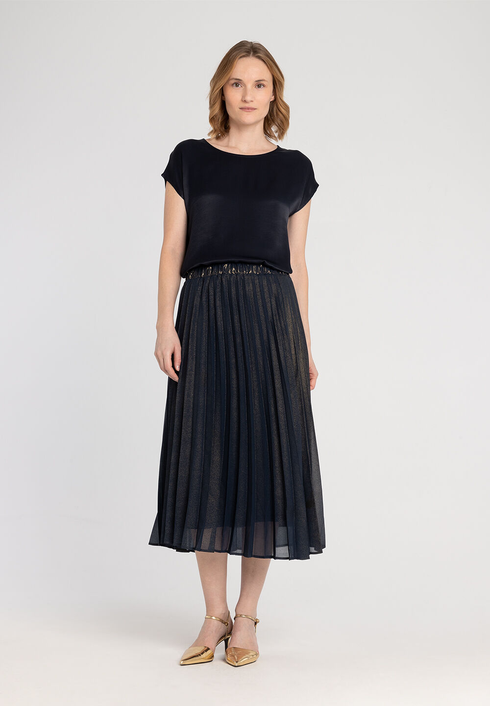 Eine Frau trägt ein MORE & MORE Oberteil aus glänzendem, dunklem Material zu einem eleganten Faltenrock. Eine Frau trägt ein MORE & MORE Oberteil aus glänzendem, dunklem Material zu einem eleganten Faltenrock.