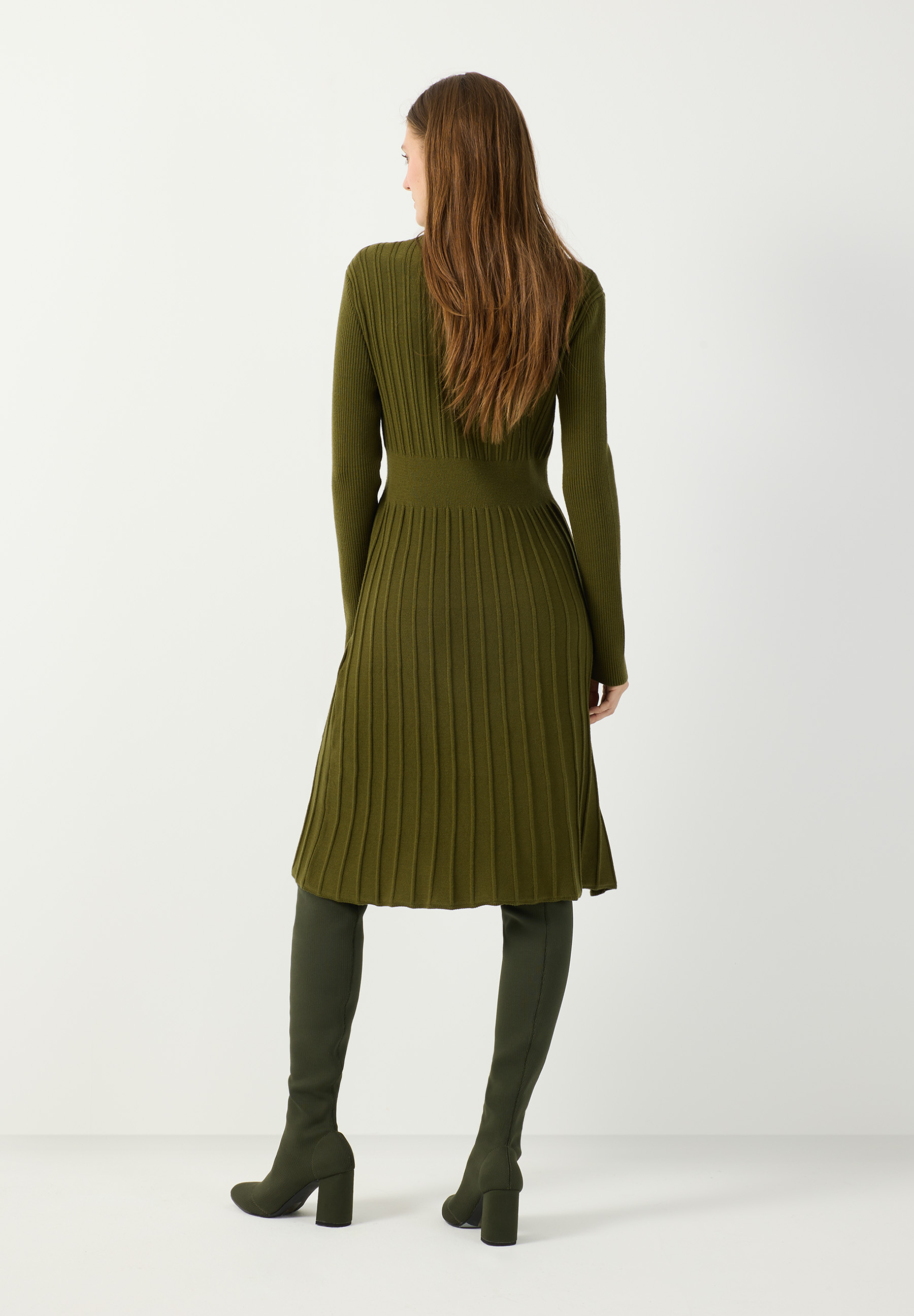 MORE & MORE grünes Rippstrick-Kleid. Eine junge Frau mit langen braunen Haaren posiert mit Blick nach links. MORE & MORE grünes Rippstrick-Kleid. Eine junge Frau mit langen braunen Haaren posiert mit Blick nach links.