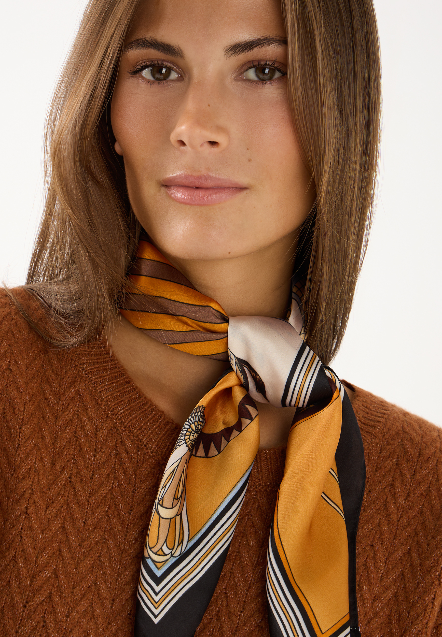 MORE & MORE Accessoire: Eine Frau trägt einen braunen Strickpullover und ein farbenfrohes, geometrisch gemustertes Halstuch.