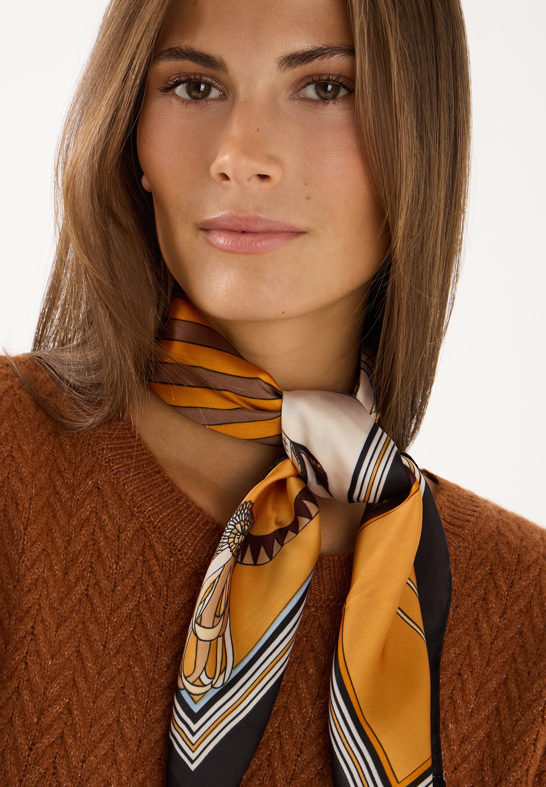 MORE & MORE Accessoire: Eine Frau trägt einen braunen Strickpullover und ein farbenfrohes, geometrisch gemustertes Halstuch.