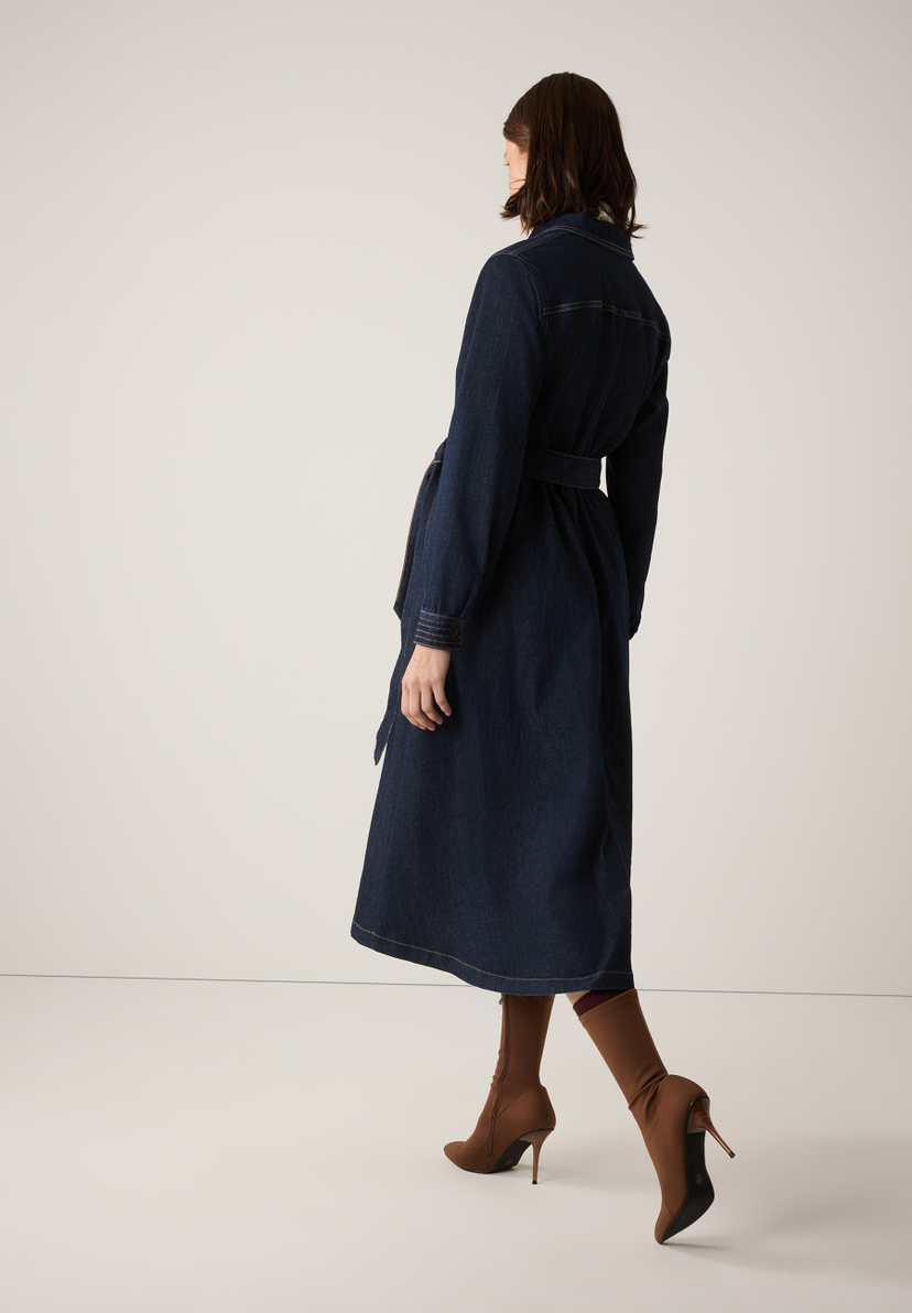 Rückansicht eines Models mit einem dunkelblauen MORE & MORE Jeanskleid mit Gürtel und braunen Stiefeln. Rückansicht eines Models mit einem dunkelblauen MORE & MORE Jeanskleid mit Gürtel und braunen Stiefeln.