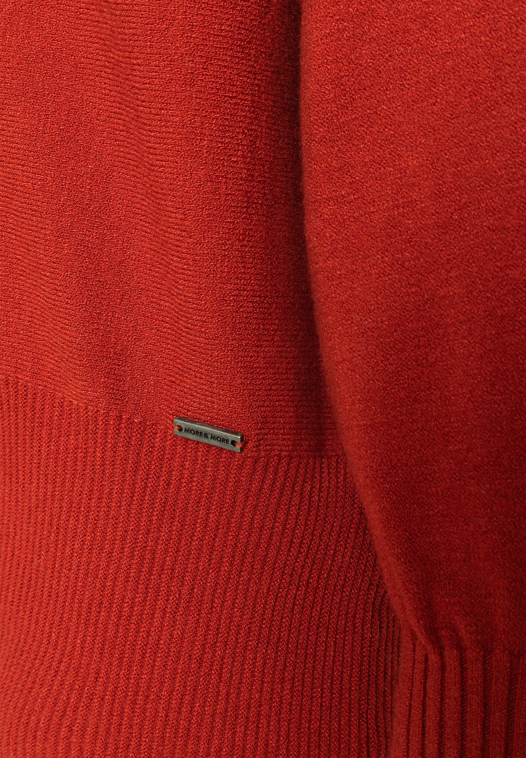 MORE & MORE Feinstrickpullover in Ziegelrot. Der Pullover hat ein geripptes Bündchen und ein kleines Markenlogo aus Metall.