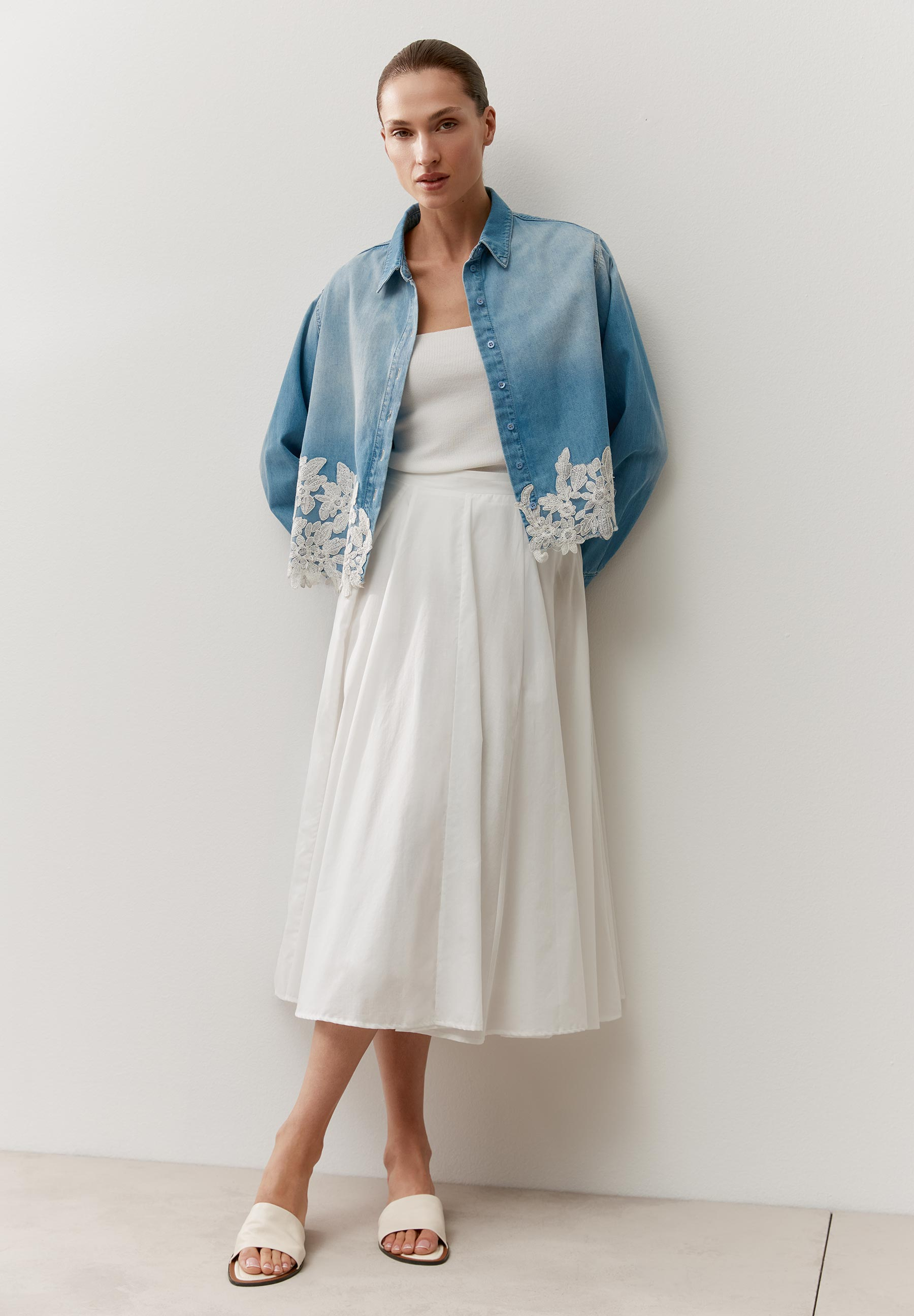 Eine Frau präsentiert MORE & MORE Oberteile, eine Jeansbluse mit Spitze und ein weißes Kleid.