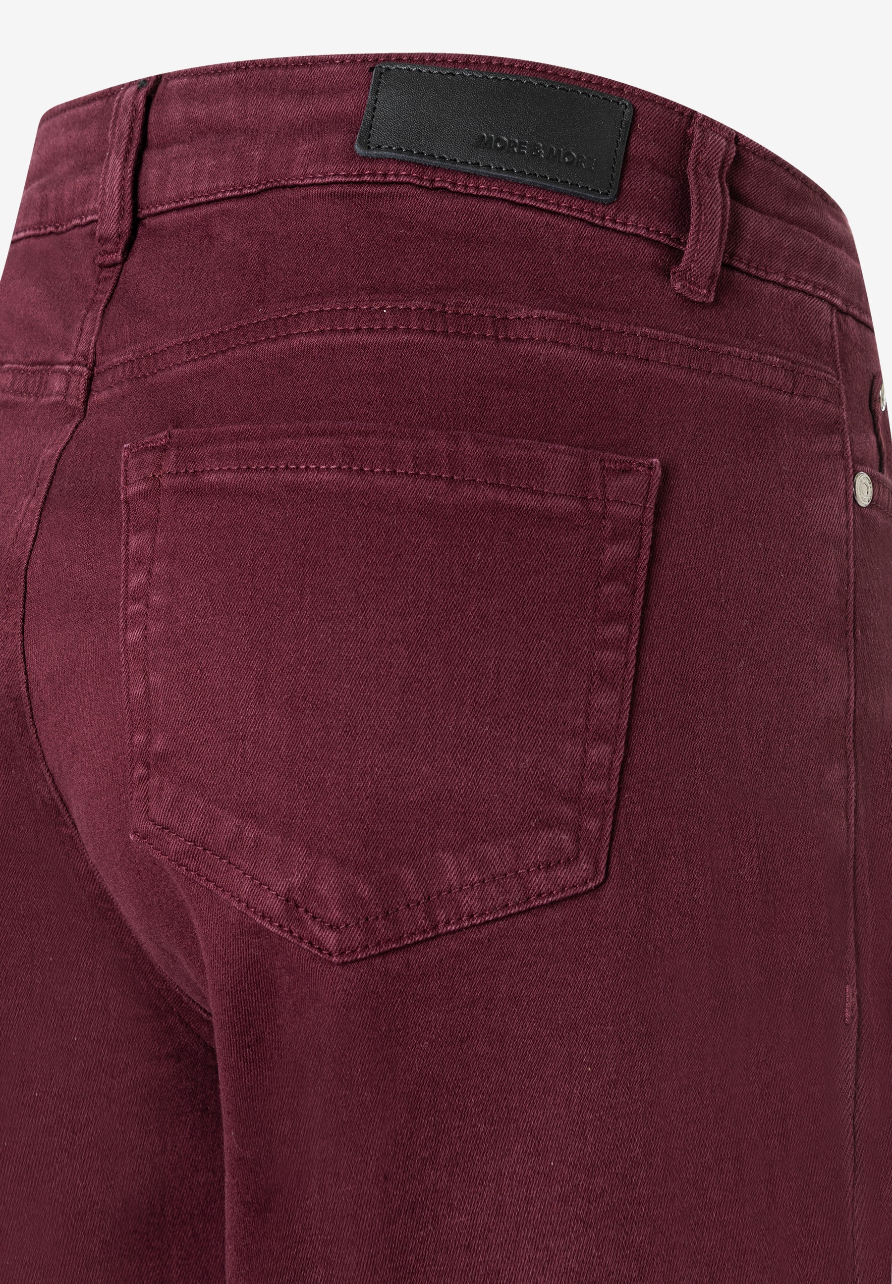 Nahaufnahme der Rückseite einer weinroten Denim-Jeans von MORE & MORE mit Gesäßtasche und Markenlabel. Nahaufnahme der Rückseite einer weinroten Denim-Jeans von MORE & MORE mit Gesäßtasche und Markenlabel.