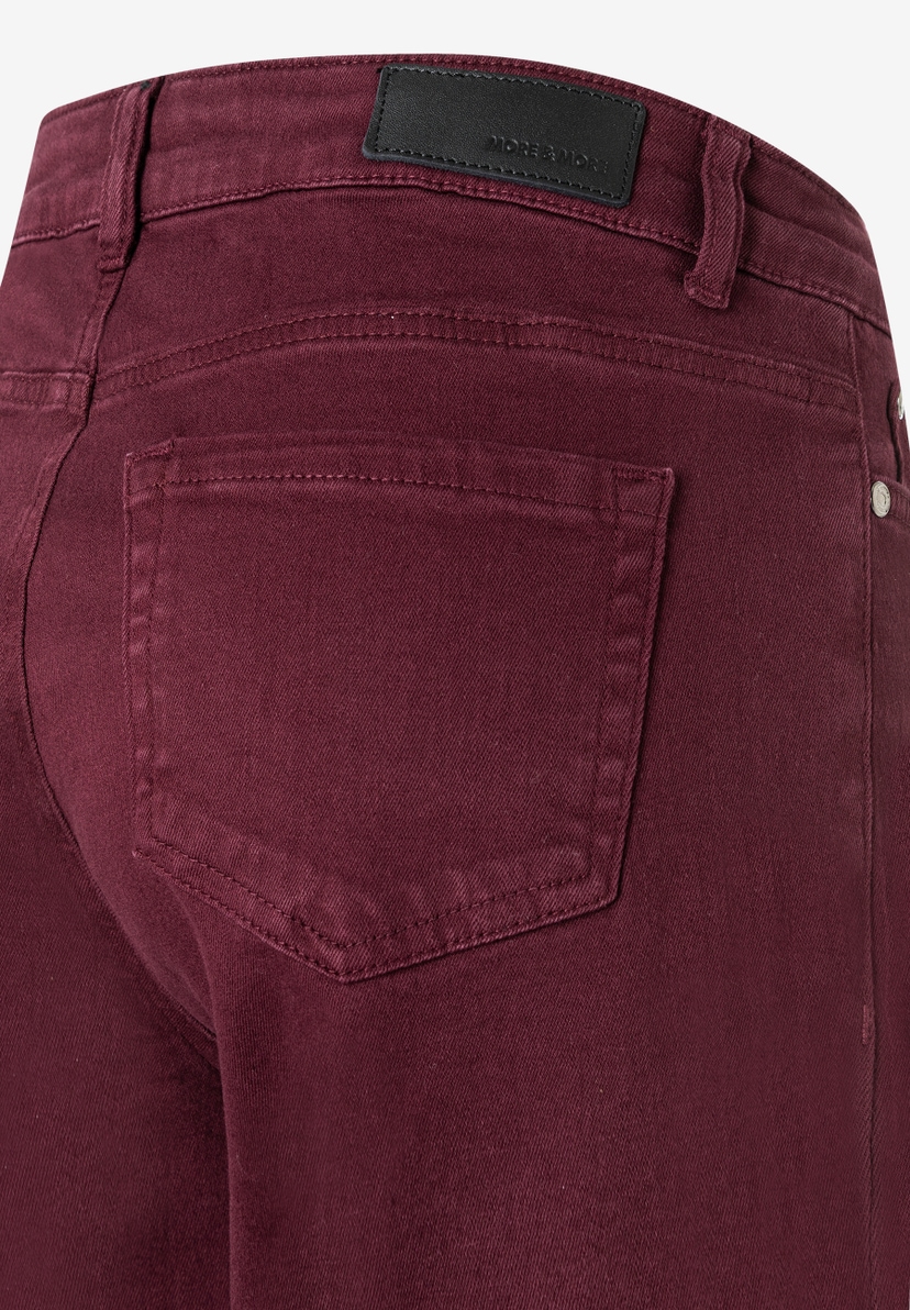 Nahaufnahme der Rückseite einer weinroten Denim-Jeans von MORE & MORE mit Gesäßtasche und Markenlabel. Nahaufnahme der Rückseite einer weinroten Denim-Jeans von MORE & MORE mit Gesäßtasche und Markenlabel.
