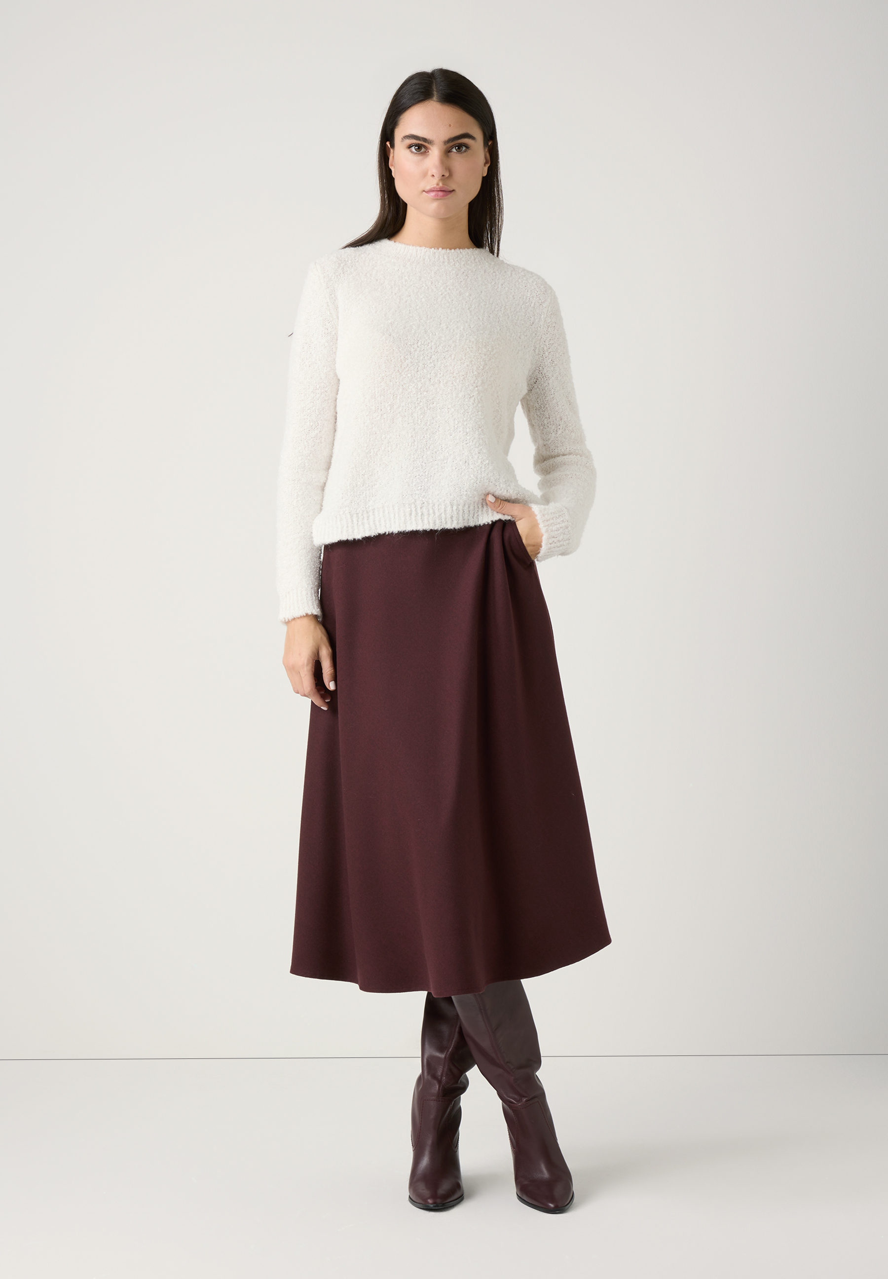 Eine Frau mit einem MORE & MORE Bouclé-Strickpullover posiert mit einer Hand in der Rocktasche. Eine Frau mit einem MORE & MORE Bouclé-Strickpullover posiert mit einer Hand in der Rocktasche.