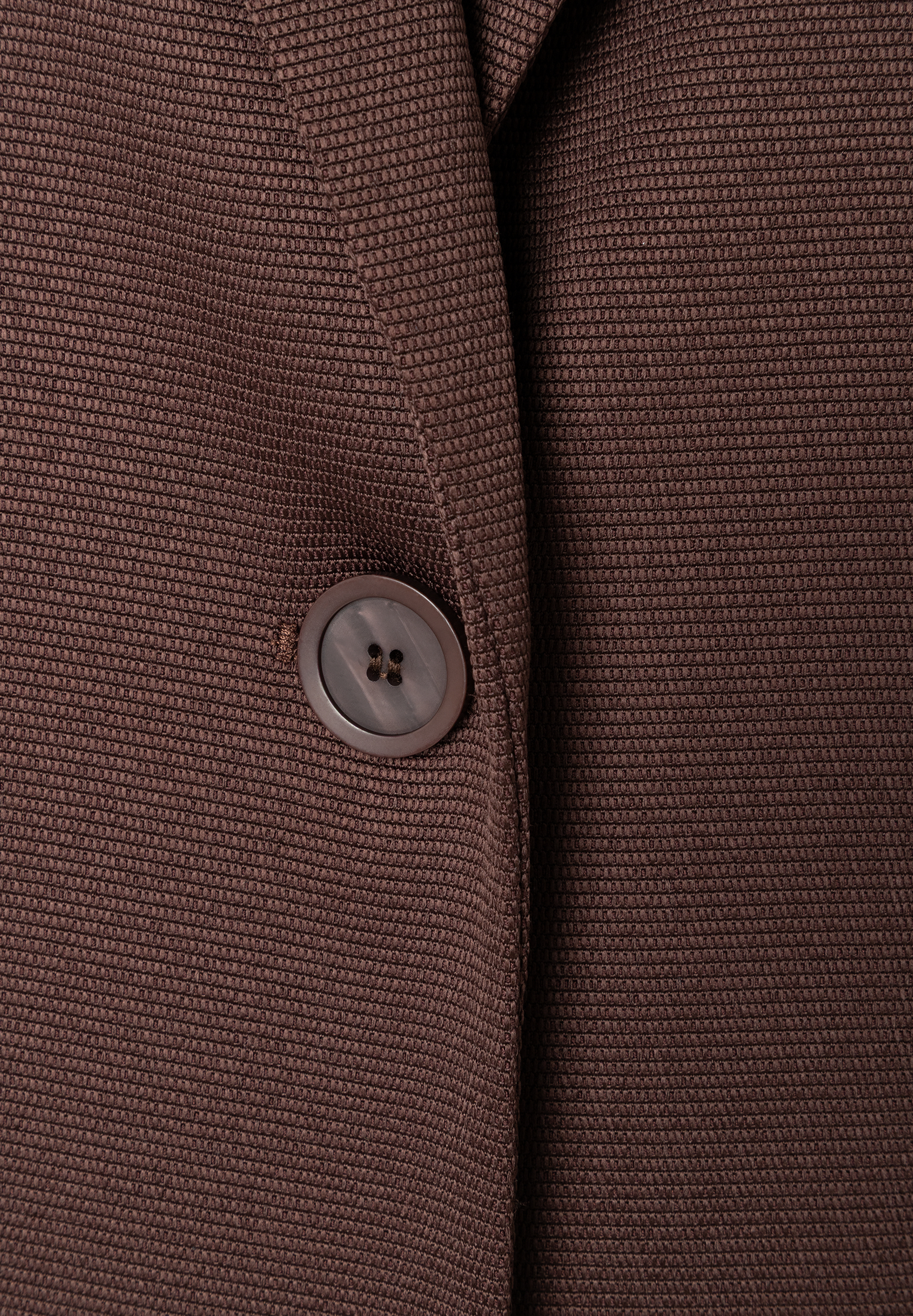 MORE & MORE Blazer: Nahaufnahme eines braunen Blazers mit Webstruktur und einem schimmernden Knopf. MORE & MORE Blazer: Nahaufnahme eines braunen Blazers mit Webstruktur und einem schimmernden Knopf.