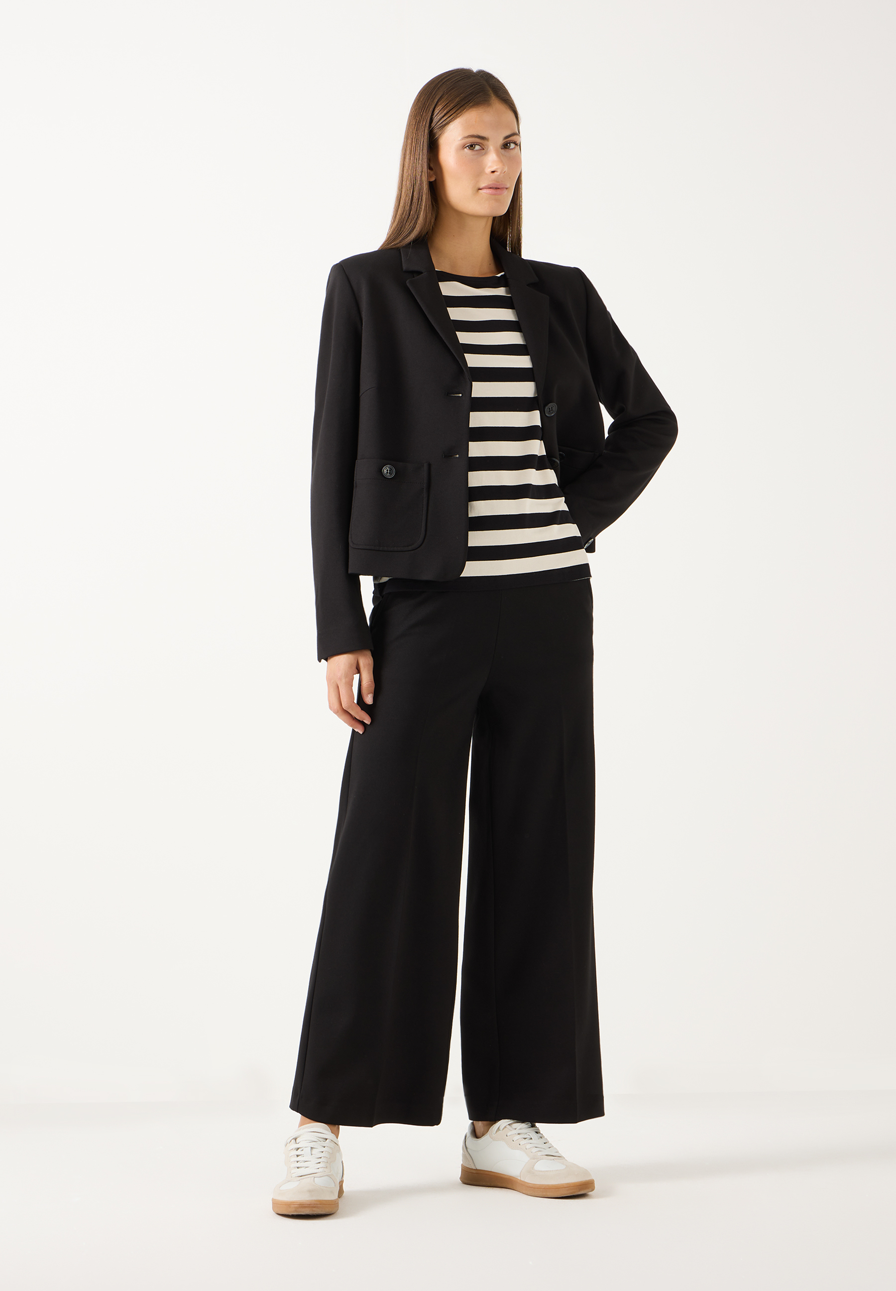 MORE & MORE Jersey-Jeans: Eine Frau steht und trägt eine braune Strickjacke und schwarze, weite Jersey-Jeans. MORE & MORE Jersey-Jeans: Eine Frau steht und trägt eine braune Strickjacke und schwarze, weite Jersey-Jeans.