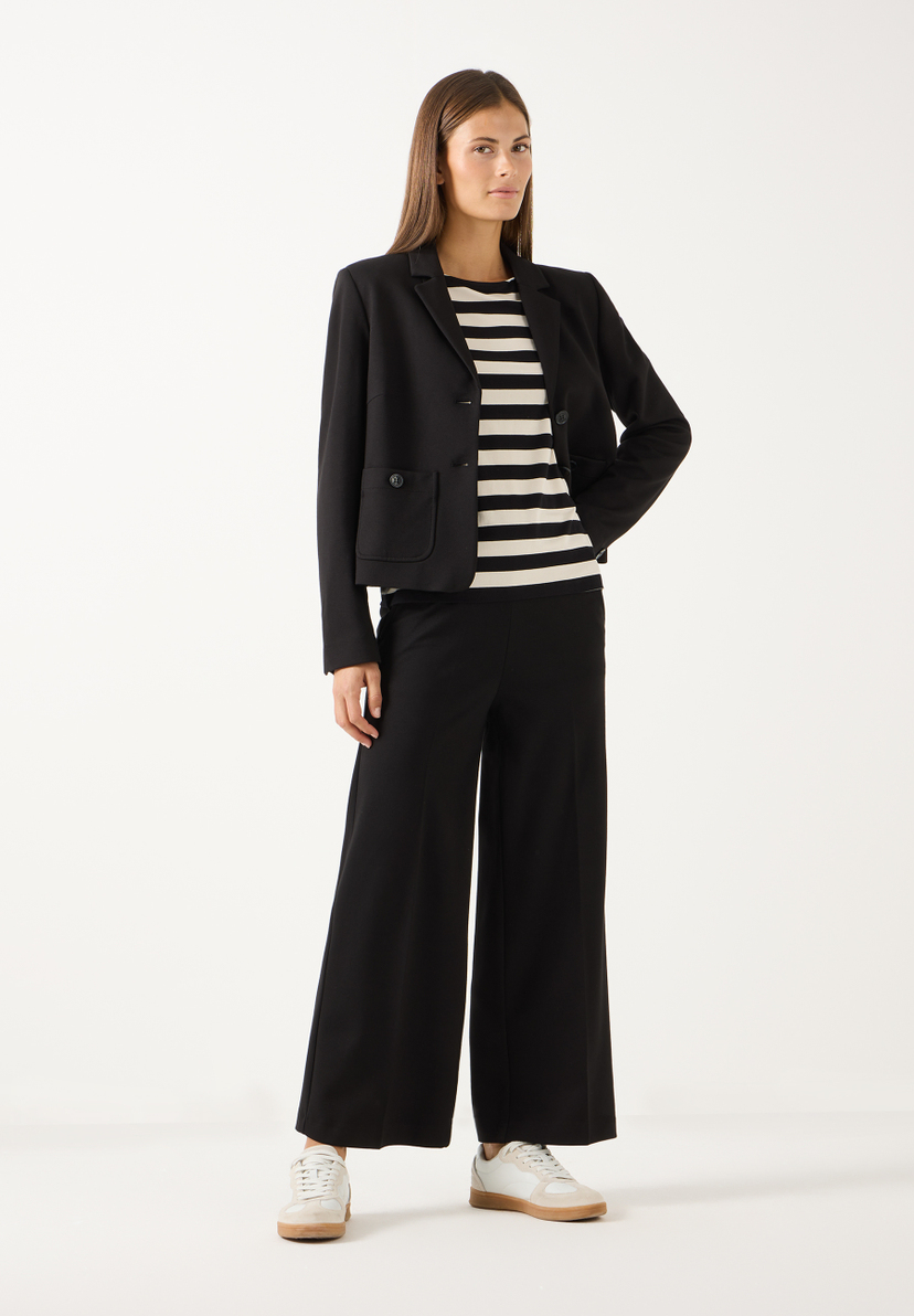 MORE & MORE Jersey-Jeans: Eine Frau steht und trägt eine braune Strickjacke und schwarze, weite Jersey-Jeans. MORE & MORE Jersey-Jeans: Eine Frau steht und trägt eine braune Strickjacke und schwarze, weite Jersey-Jeans.