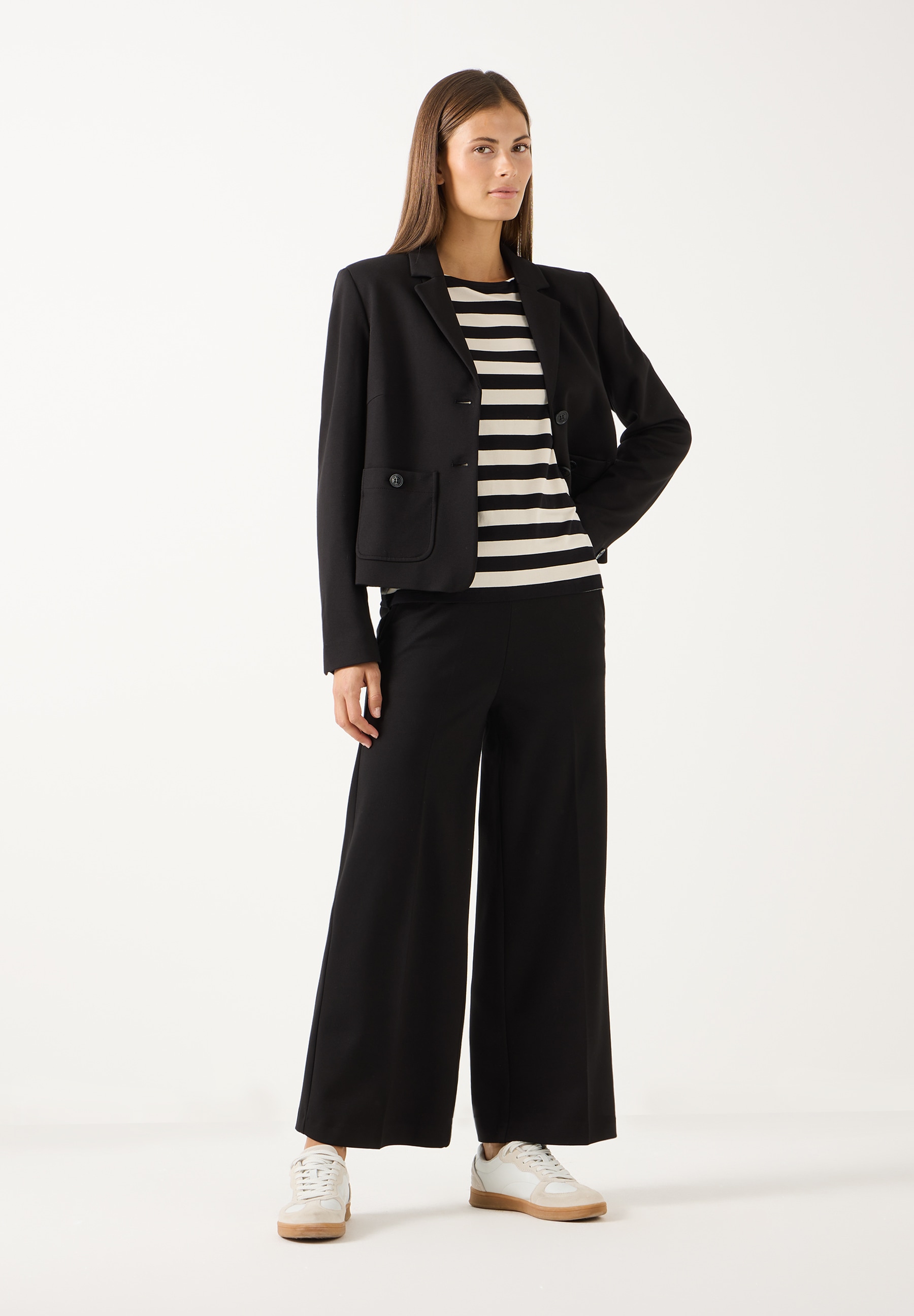 MORE & MORE Jersey-Jeans: Eine Frau steht und trägt eine braune Strickjacke und schwarze, weite Jersey-Jeans. MORE & MORE Jersey-Jeans: Eine Frau steht und trägt eine braune Strickjacke und schwarze, weite Jersey-Jeans.