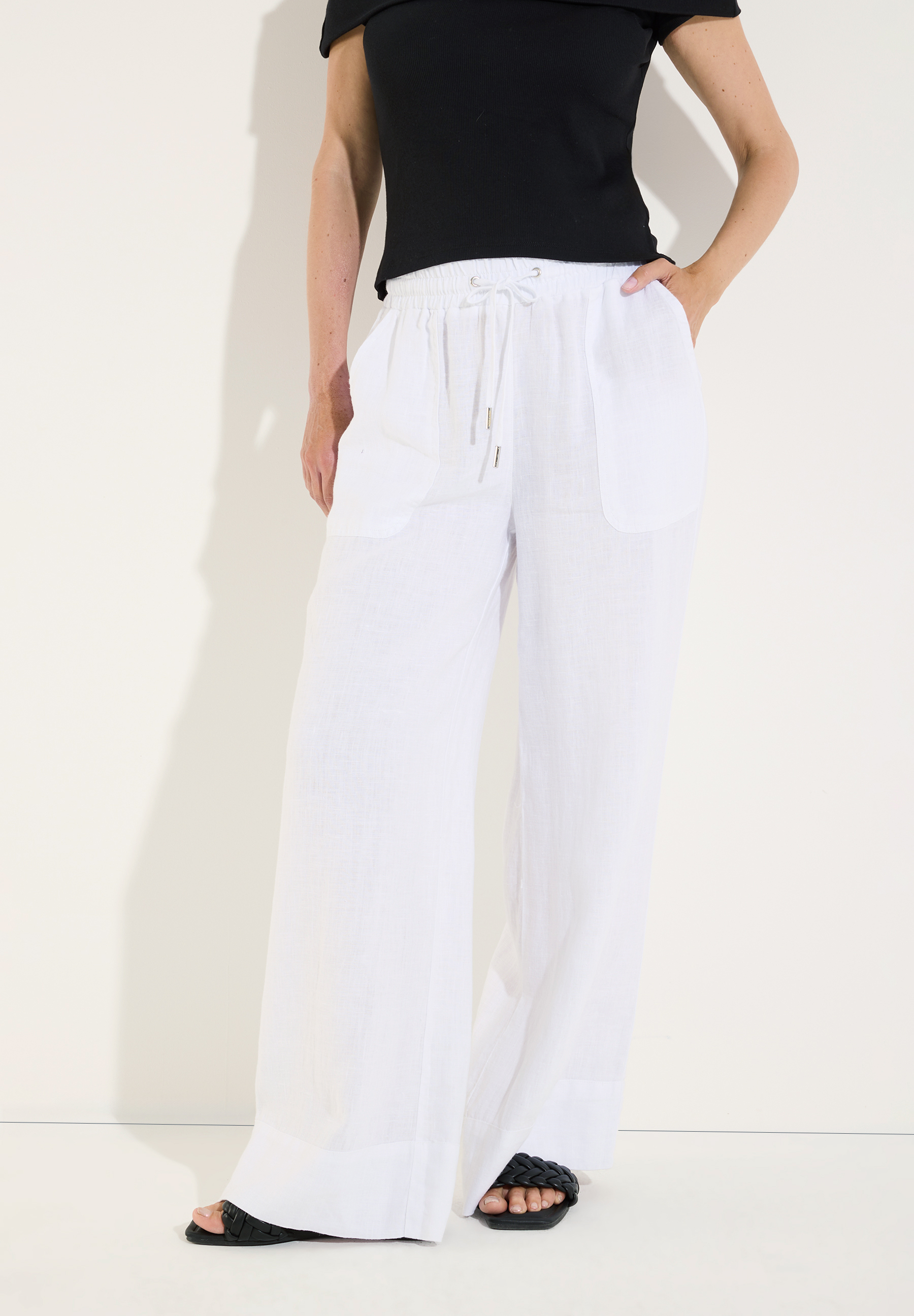 MORE & MORE Leinenhose, weiß, mit weitem Bein, Kordelzug und 2 Taschen, getragen mit schwarzem Off-Shoulder-Top und schwarzen Sandalen.