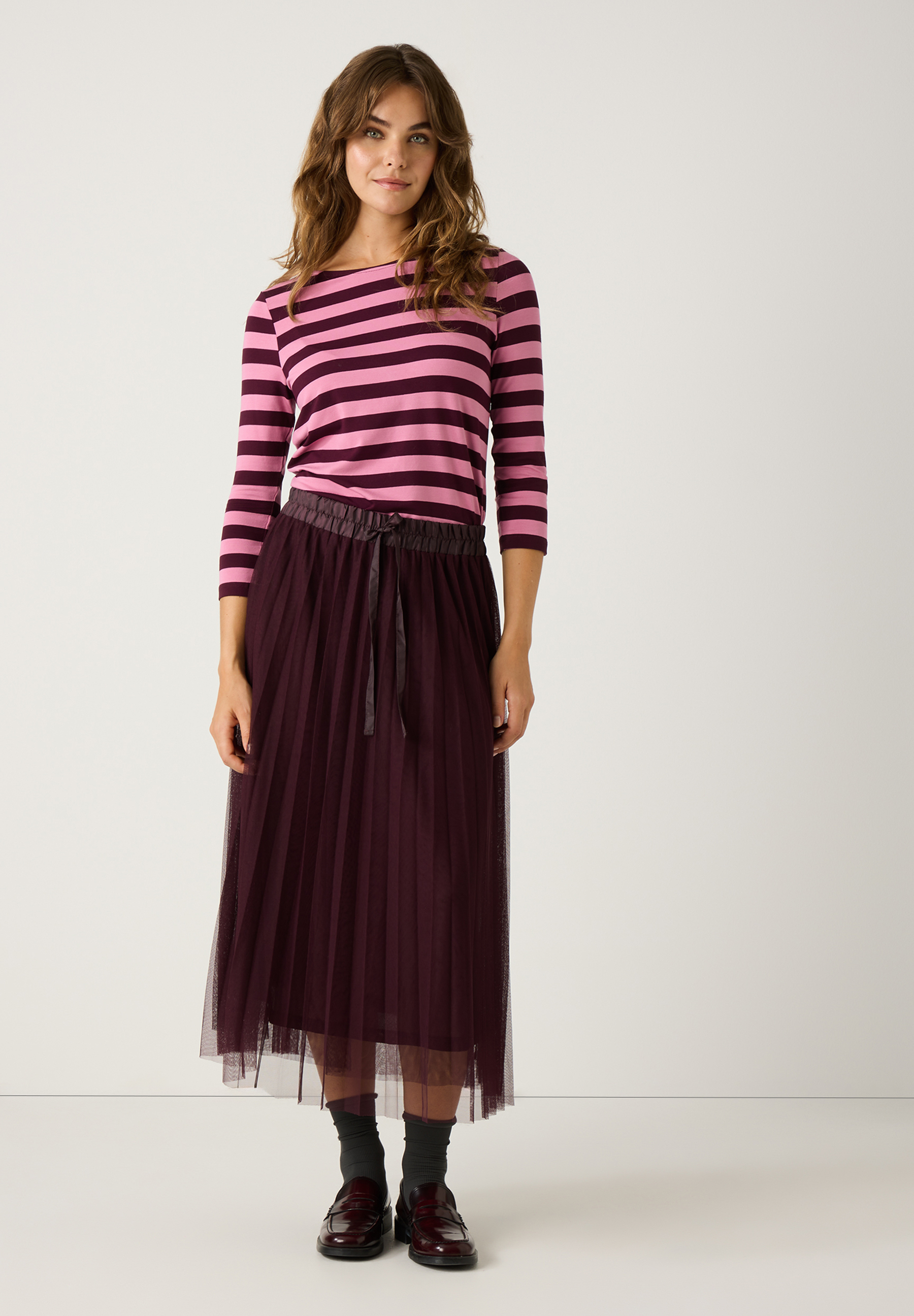 Eine Frau in einem gestreiften Oberteil und einem MORE & MORE Mesh-Rock posiert vor einem weißen Hintergrund. Eine Frau in einem gestreiften Oberteil und einem MORE & MORE Mesh-Rock posiert vor einem weißen Hintergrund.