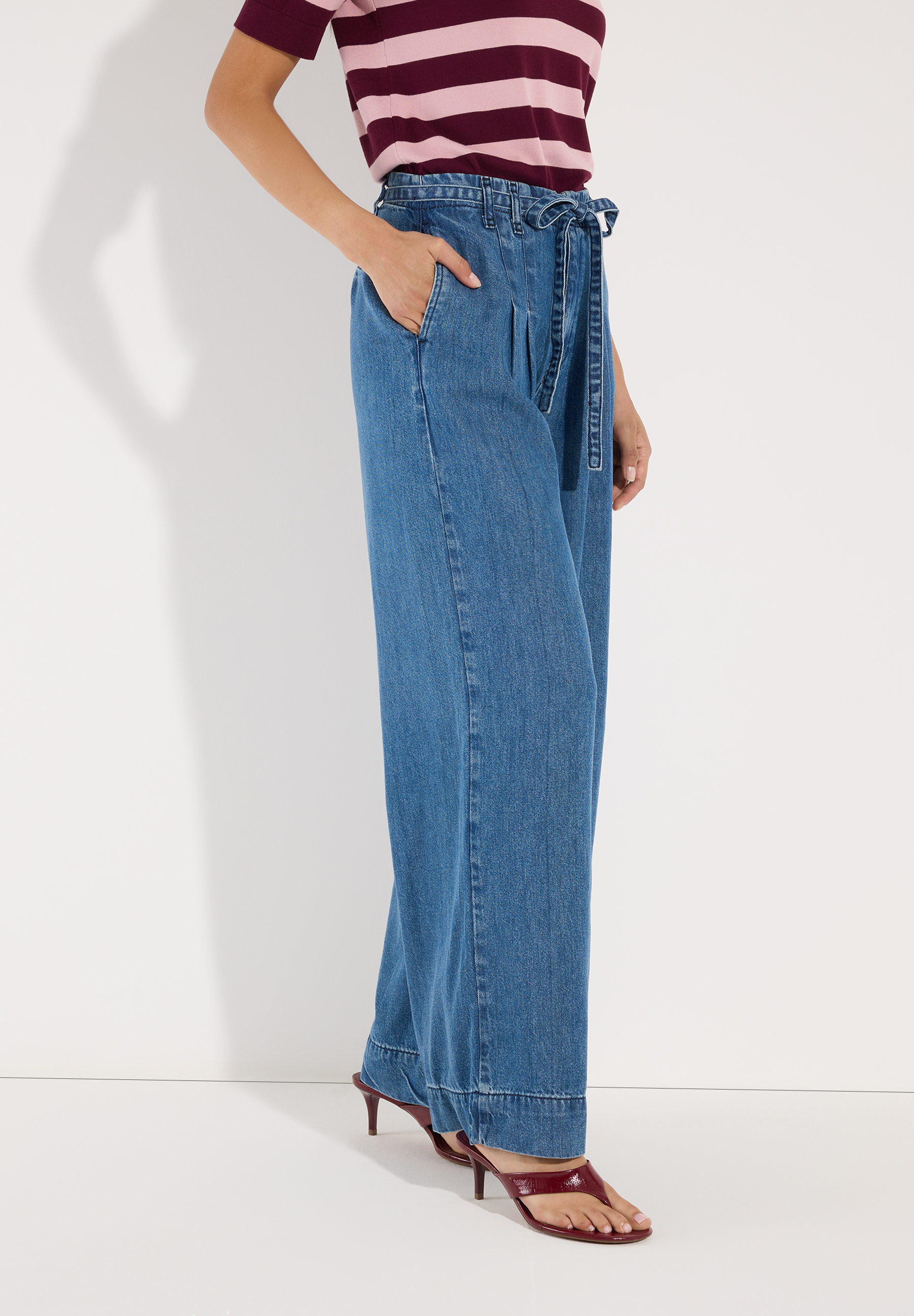 MORE & MORE Jeans: Junge Frau sitzt seitlich mit verschränkten Beinen und trägt eine MORE & MORE Jeans aus Denim. MORE & MORE Jeans: Junge Frau sitzt seitlich mit verschränkten Beinen und trägt eine MORE & MORE Jeans aus Denim.