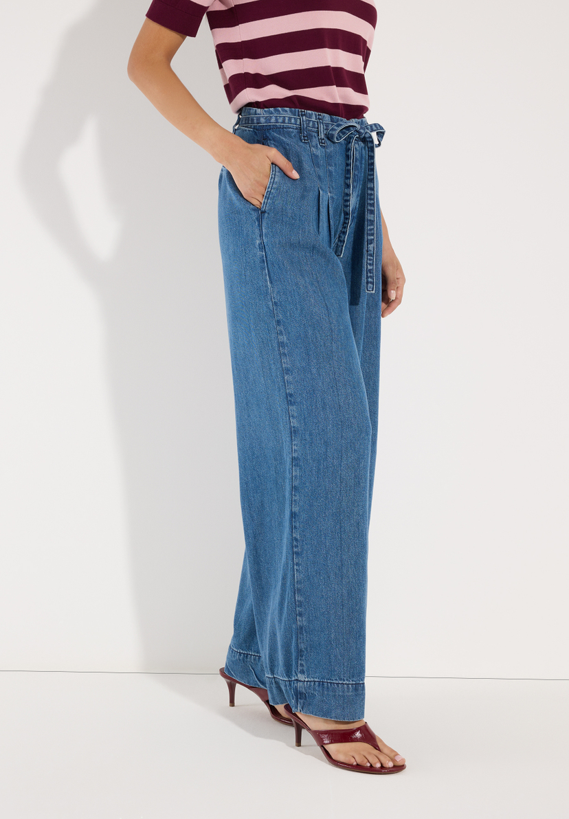 MORE & MORE Jeans: Junge Frau sitzt seitlich mit verschränkten Beinen und trägt eine MORE & MORE Jeans aus Denim. MORE & MORE Jeans: Junge Frau sitzt seitlich mit verschränkten Beinen und trägt eine MORE & MORE Jeans aus Denim.