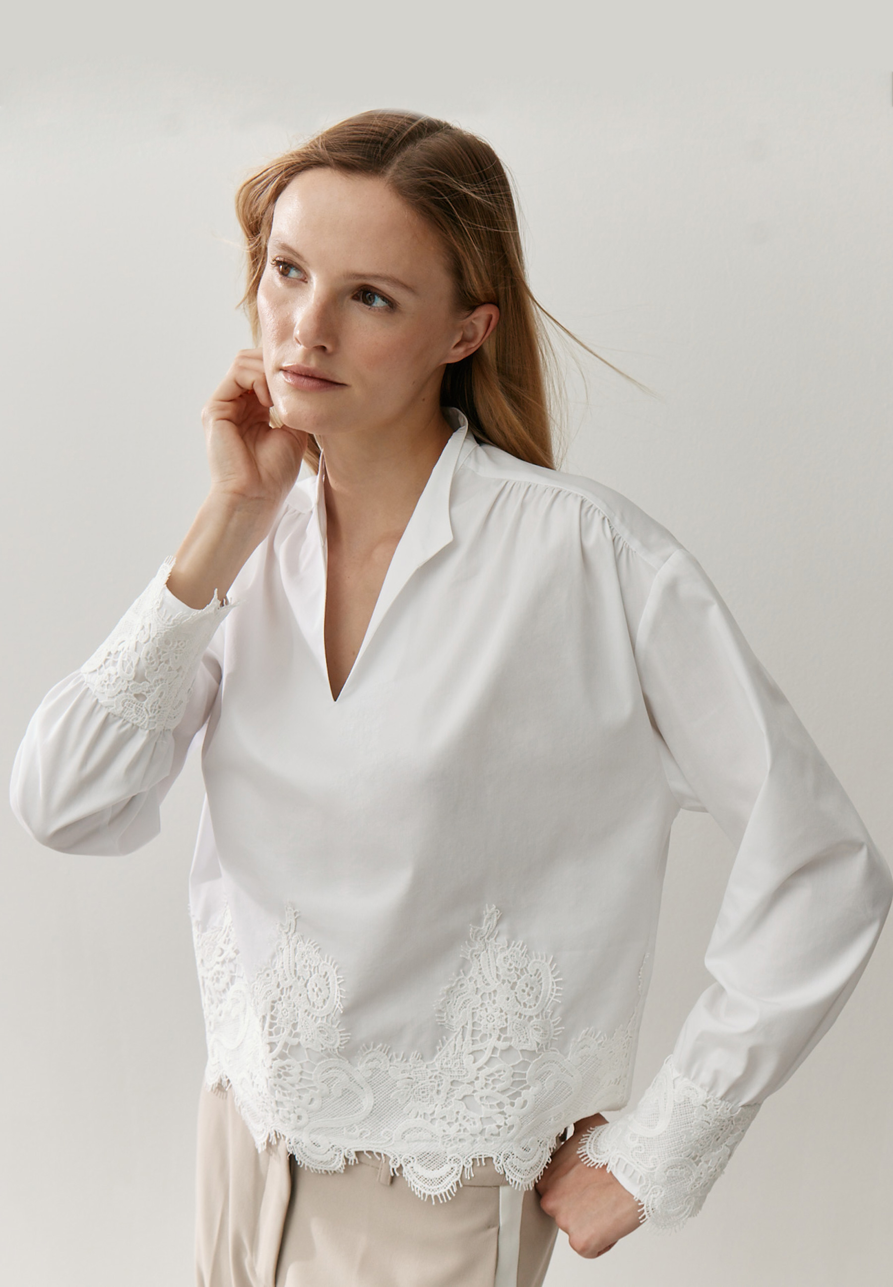 Eine Frau, die eine weiße MORE & MORE Bluse mit Spitzendetails trägt. Eine Frau, die eine weiße MORE & MORE Bluse mit Spitzendetails trägt.