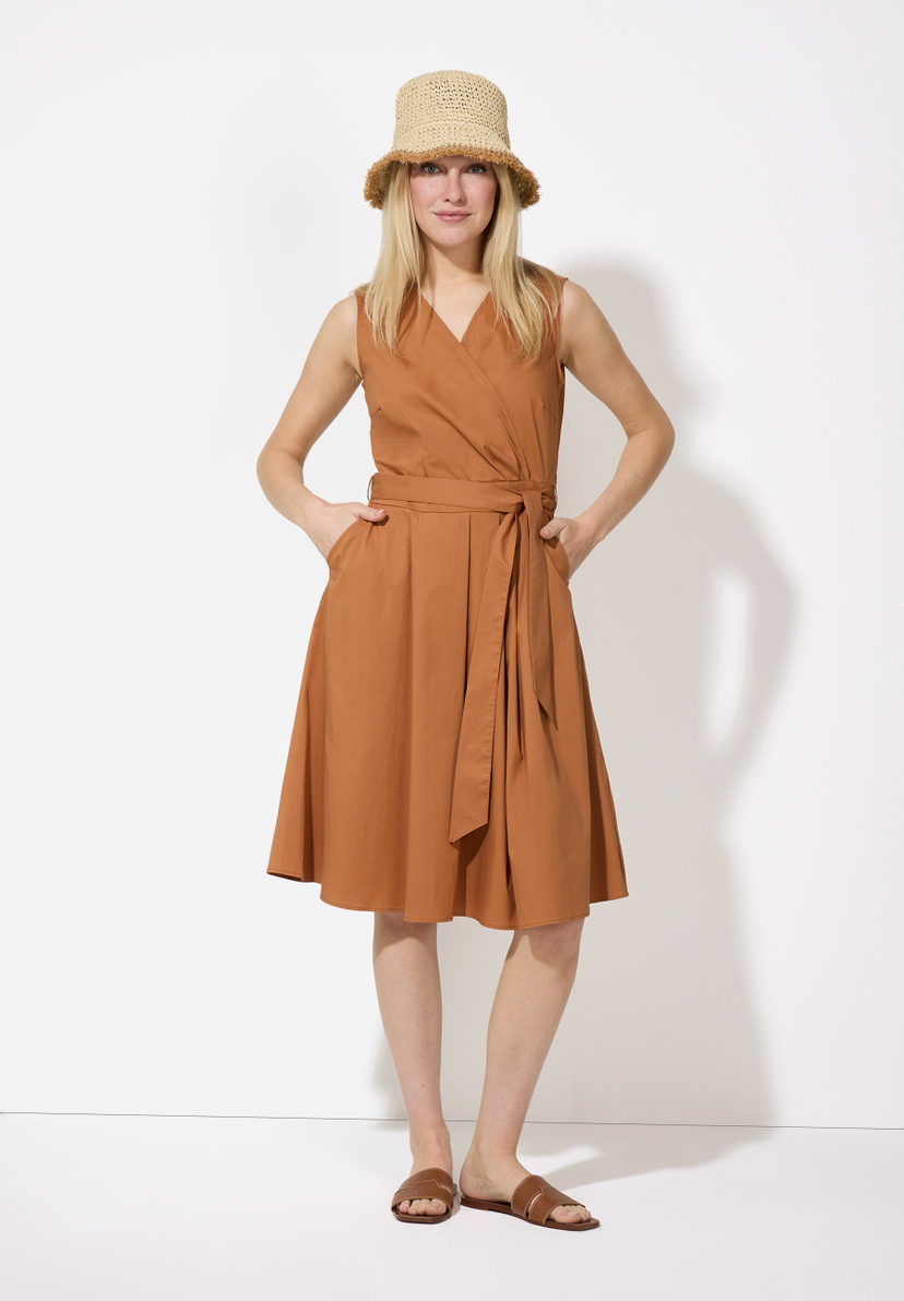 Eine Frau mit einem MORE & MORE Strohhut, ein ärmelloses Kleid in einem Braunton, mit Gürtel und braunen Ledersandalen. Eine Frau mit einem MORE & MORE Strohhut, ein ärmelloses Kleid in einem Braunton, mit Gürtel und braunen Ledersandalen.